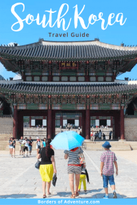 A woman holding a blue umbrella, with three family members, walks towards the two-tiered boat roof entrance of the imperial palace in South Korea