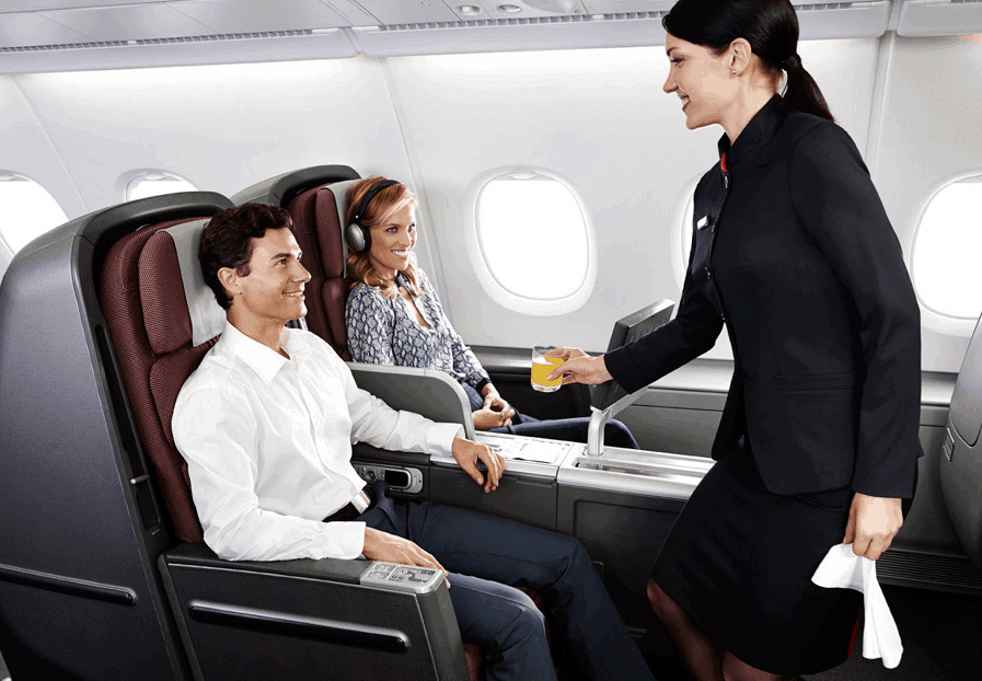 A member of cabin crew dressed in black serves a male and female passenger in large business class seats on board a Qantas A380 flight.