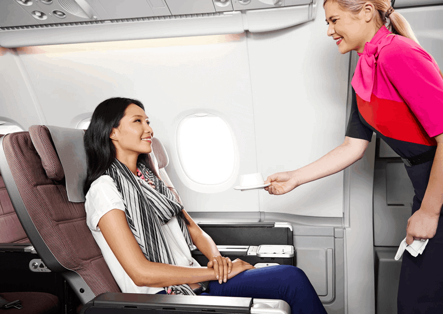 A member of cabin crew dressed in a pink, red and black outfit serves a female passenger a drink in a white teacup on board a Qantas A380 flight.