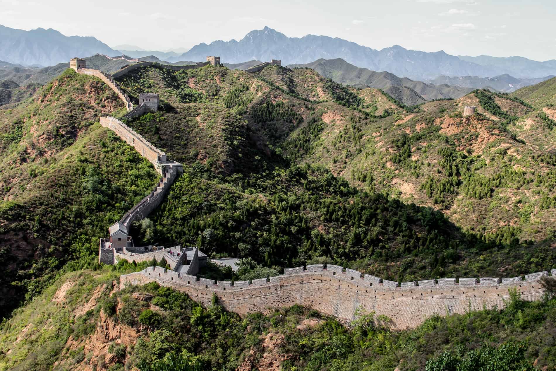 The Great Wall of China cutting a path through rolling green hills. 