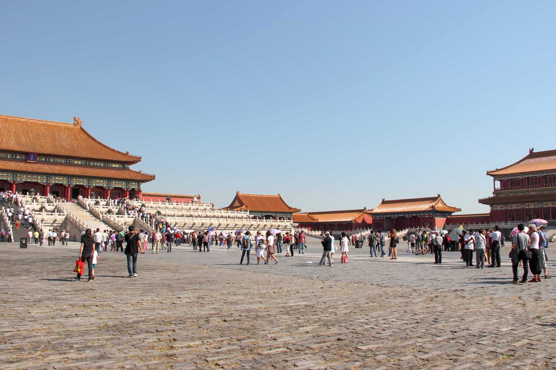 A mass of people of an open square surrounded by traditional Chinese pagada buildings of a former imperial palace complex. 