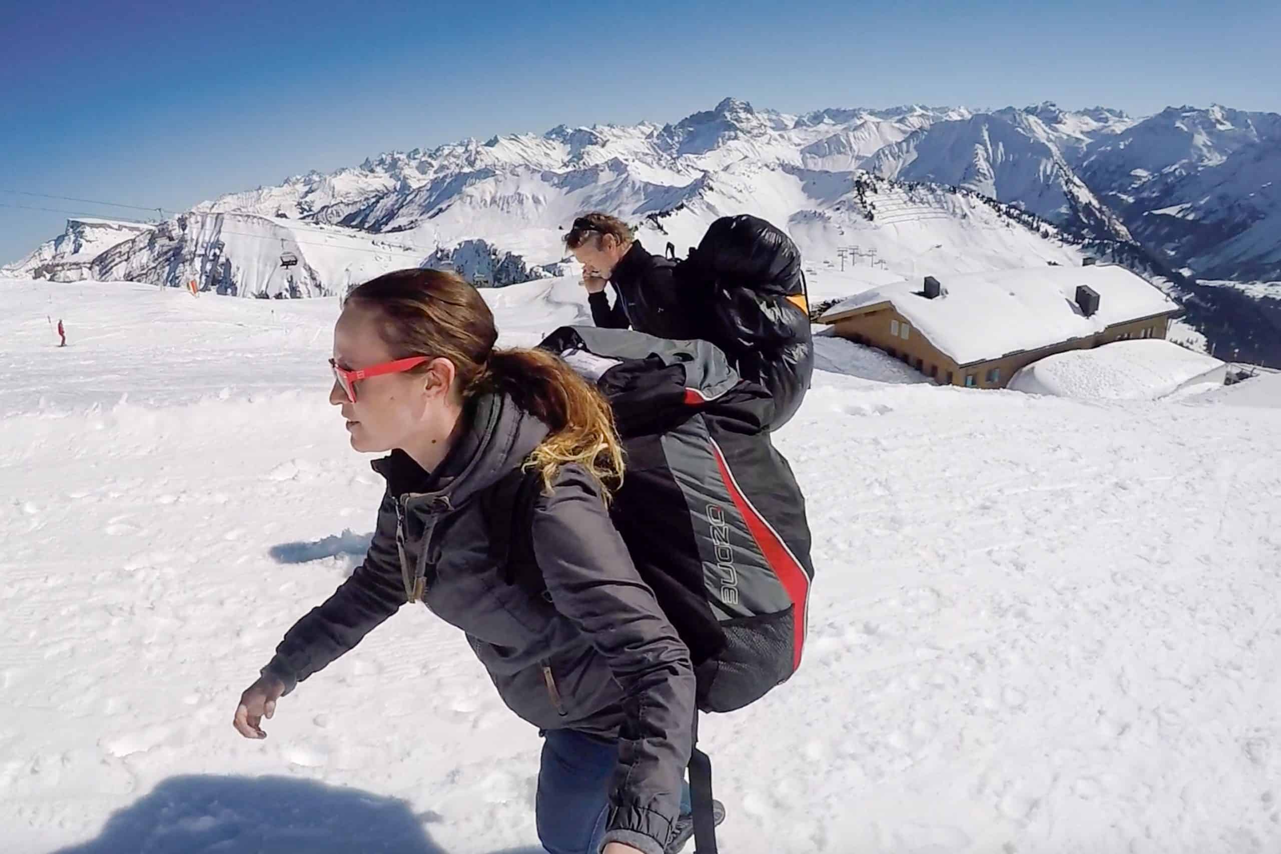 A man and a woman, both wearing large backpacks walk up a snowy mountain path in the Austrian Alps