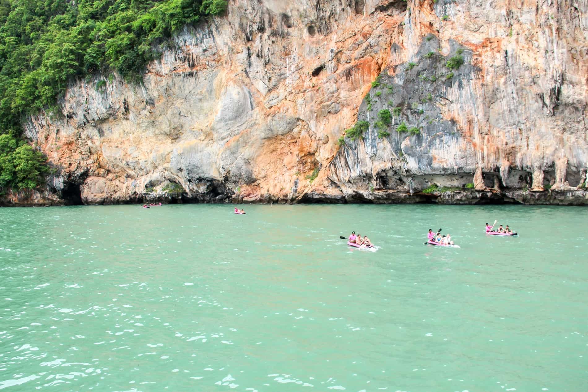 People canoeing in the emerald green water of a Thai island.