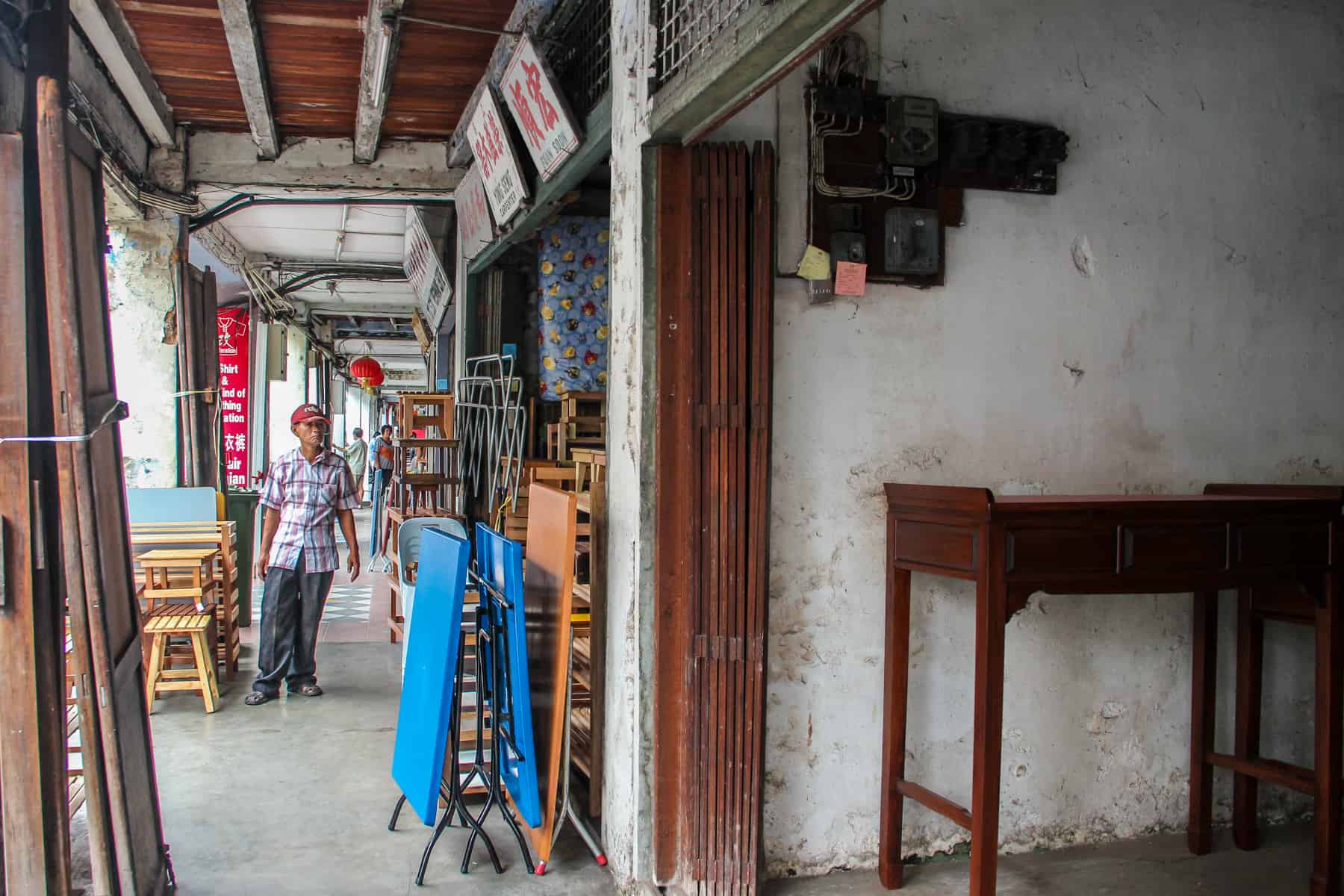 An elderly man stands in a long, white corridor that conceals handicraft and carpenter workshops in Kuching