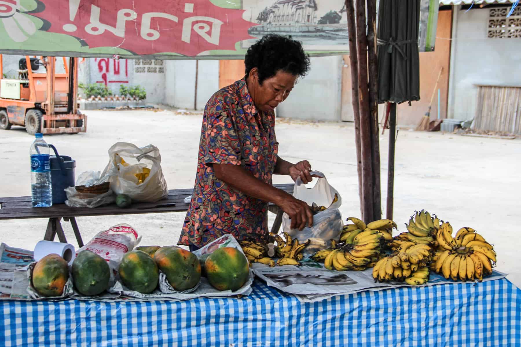 A Thai lady selling bananas and watermelons on a blue covered stall in Bangkok