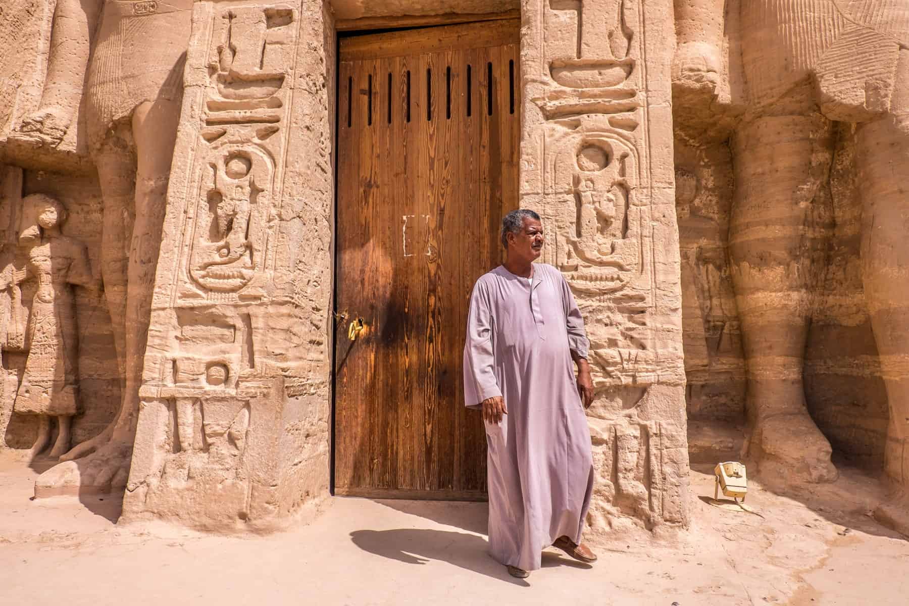 An Egyptian temple guard in a white tunic robe stands outside the carved columns at Abu Simbel Temple near Aswan