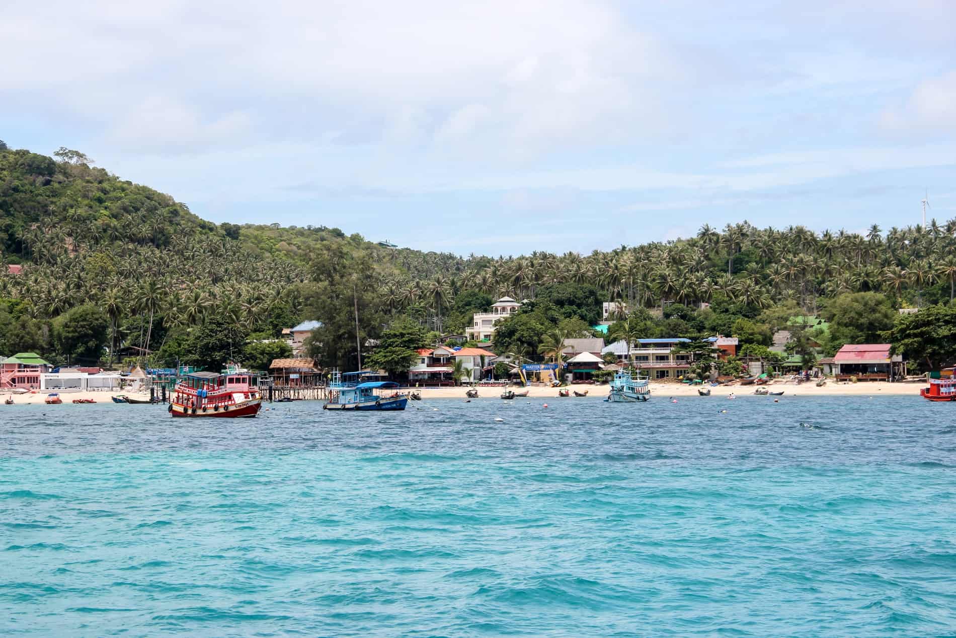 Boats on the bright blue waters of the jungle backed coastline of Koh Phi Phi island, Thailand. 