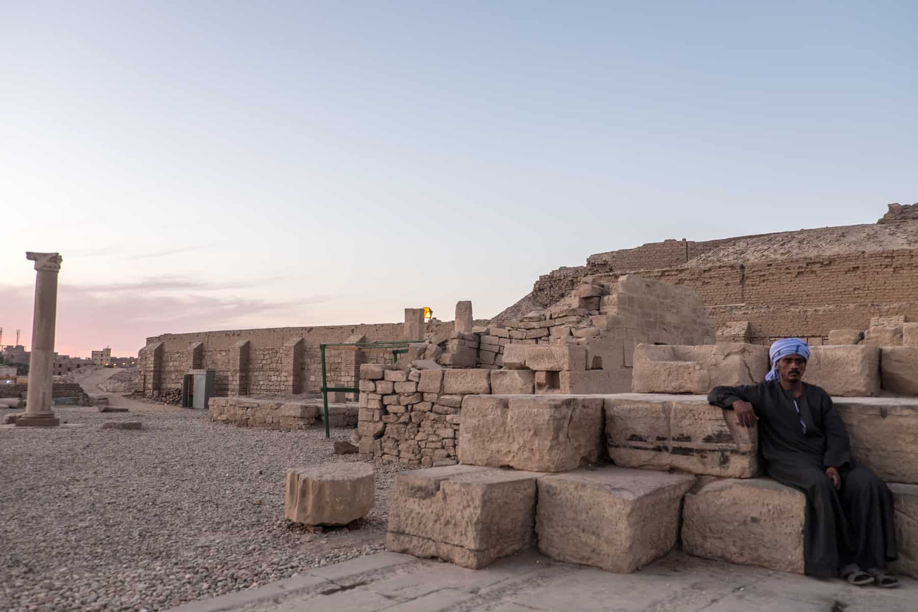 Egyptian Kom Ombo temple guard sits on one of the temple stone blocks at sunset