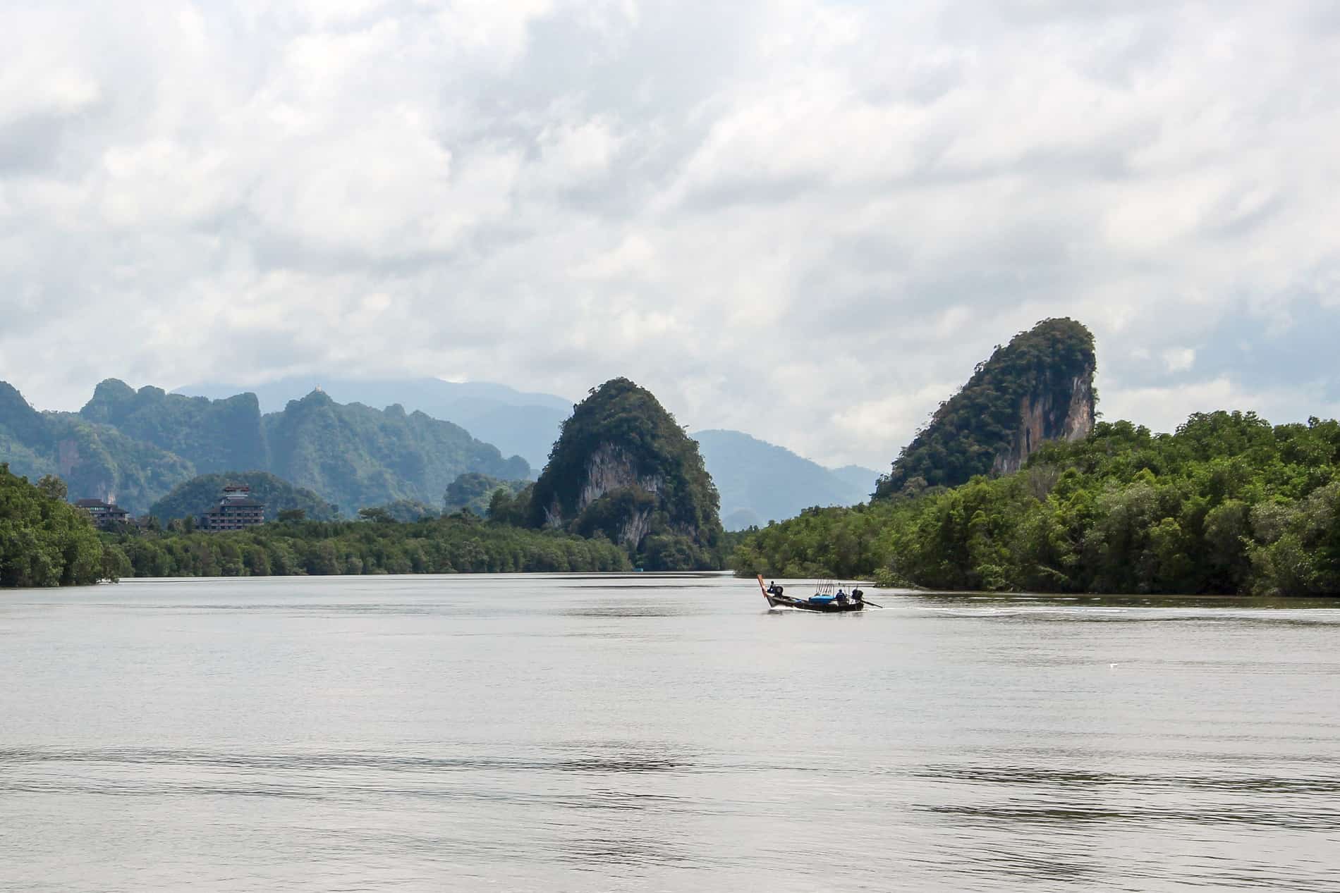 A boat on the stillwater of Krabi River in Thailand, backed by forest and limestone formations.