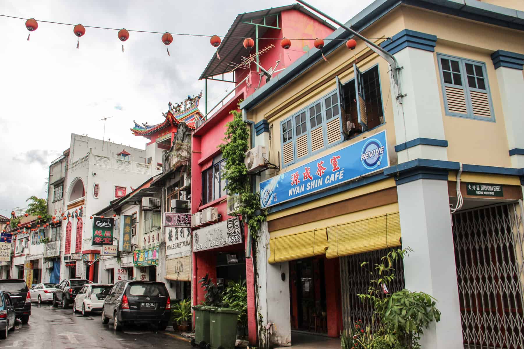 Colonial and Chinese style architecture mix on a street front in Kuching, where buildings are painted in yellow, blue and pink and decorated with Chinese lanterns