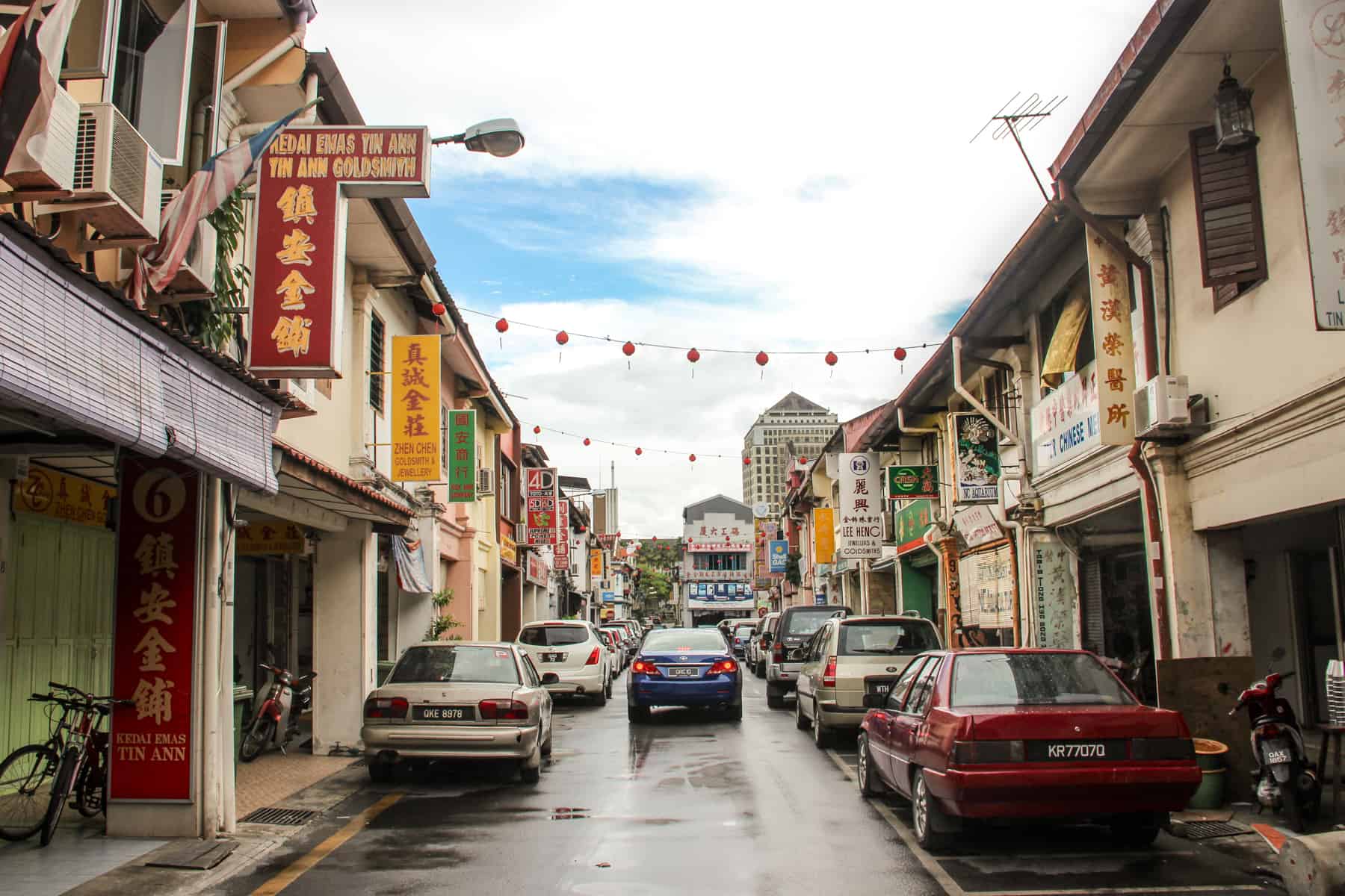 Chinese shop signs protrude from the beige buildings lining a typical shopping street in Old Town Kuching
