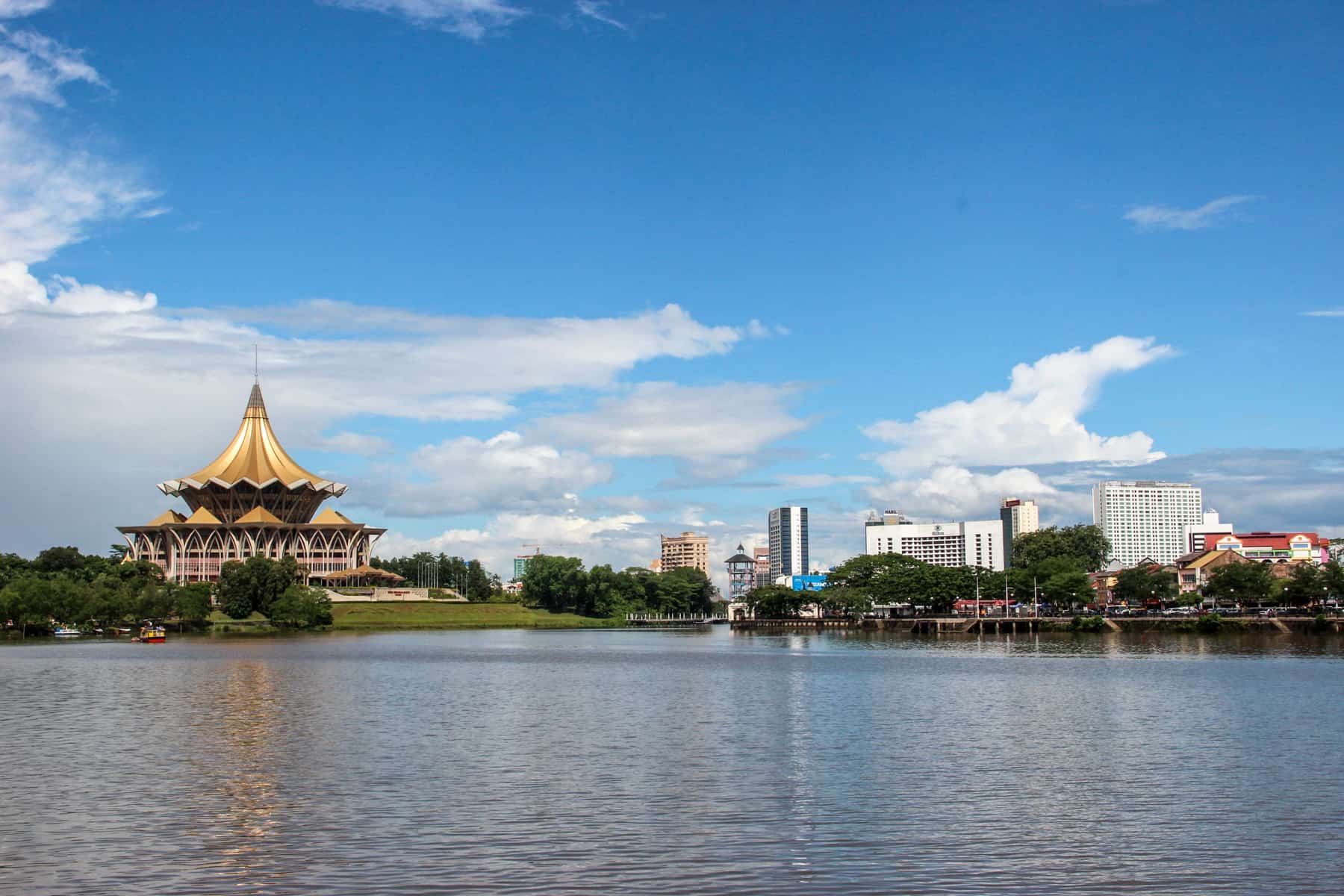 A golden domed building on the left and lowrise white buildings on the right line the Sarawak Rick in Kuching Borneo