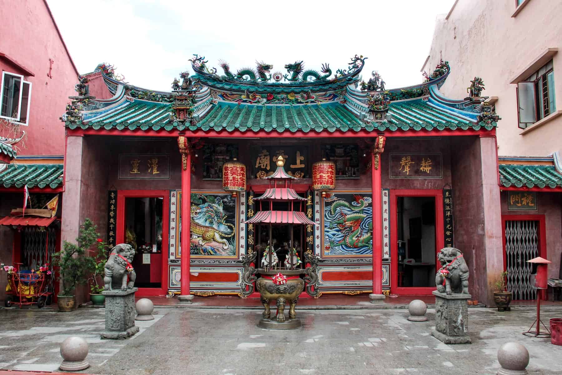 A turquoise upside down bat roof with dragon structures and the red columns with lanterns and dragon wall paintings mark the entrance of Kuching's Oldest Temple of Tua Pek Kong