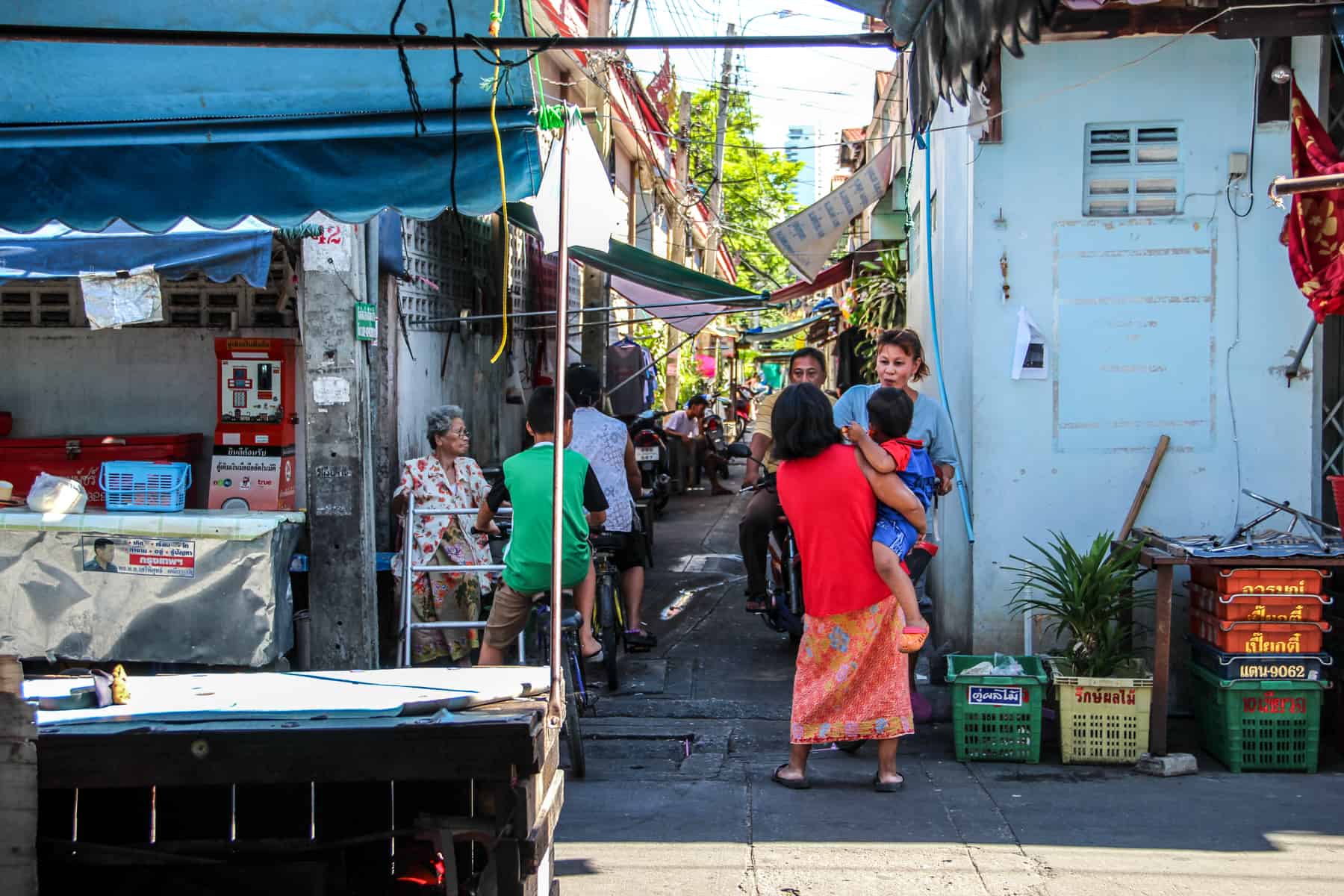 Thai men and women gather to talk to a narrow alleyway in a Bangkok neighbourhood, found on a bike tour