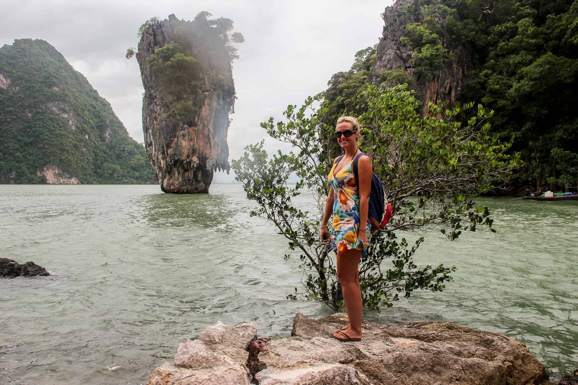 A woman stands ona. rock in front of a limestone formation known as James Bond Island in Thailand. 