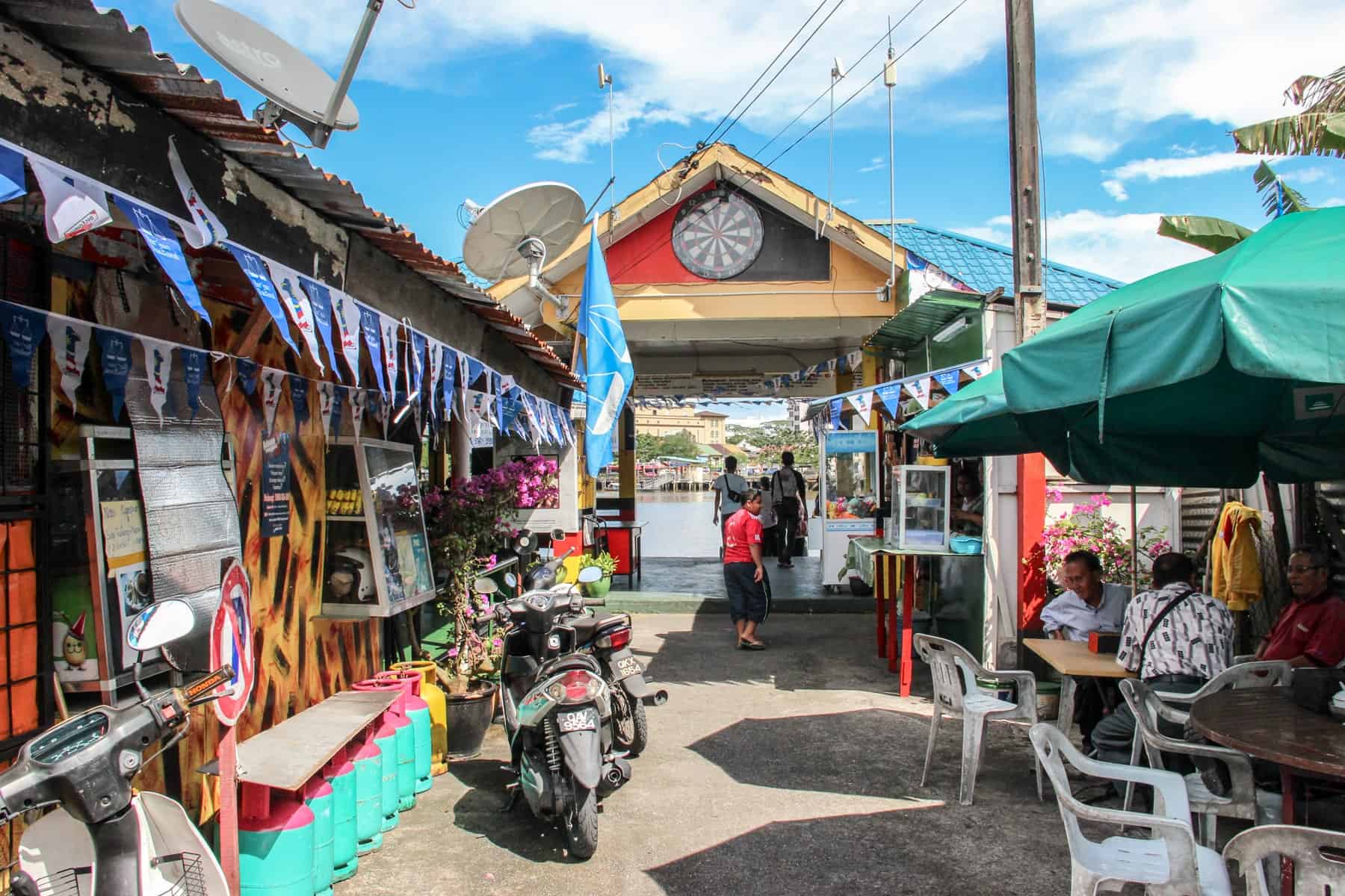 The red, yellow and turquoise painted passenger dock on the Sarawak River in Kuching. People sit and eat next to store fronts