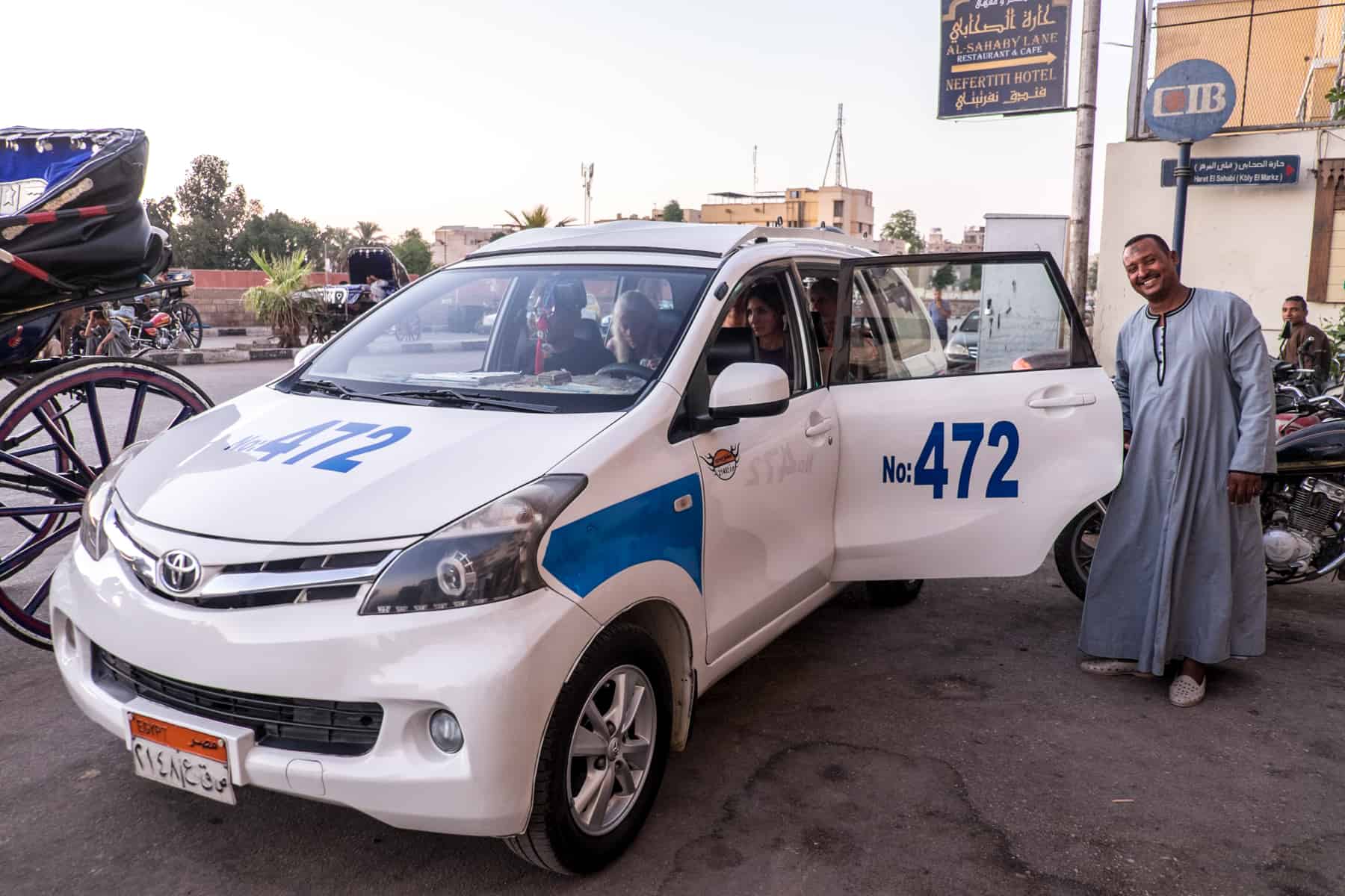 An Egyptian man prudly stands with his white and blue taxi in Luxor, Egypt