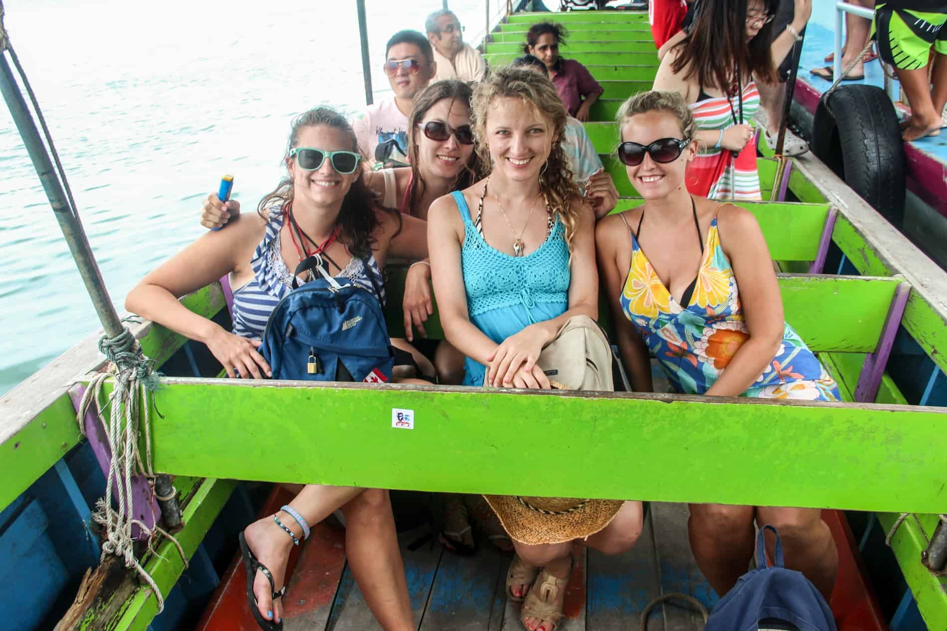 A group of friends Thailand island hopping by ferry, smiling at the camersa from green seats.