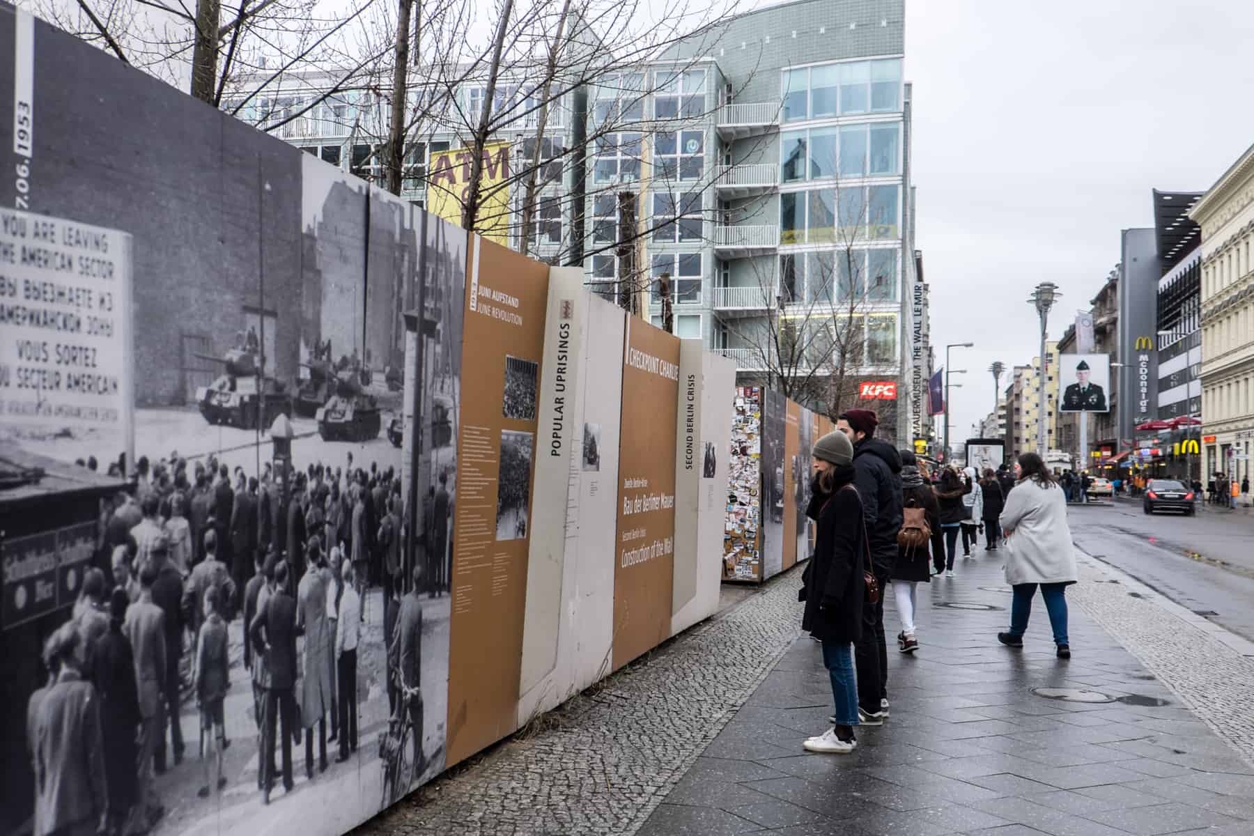 People stand in the street reading large orange and white history information boards about the Berlin Wall and the Cold War