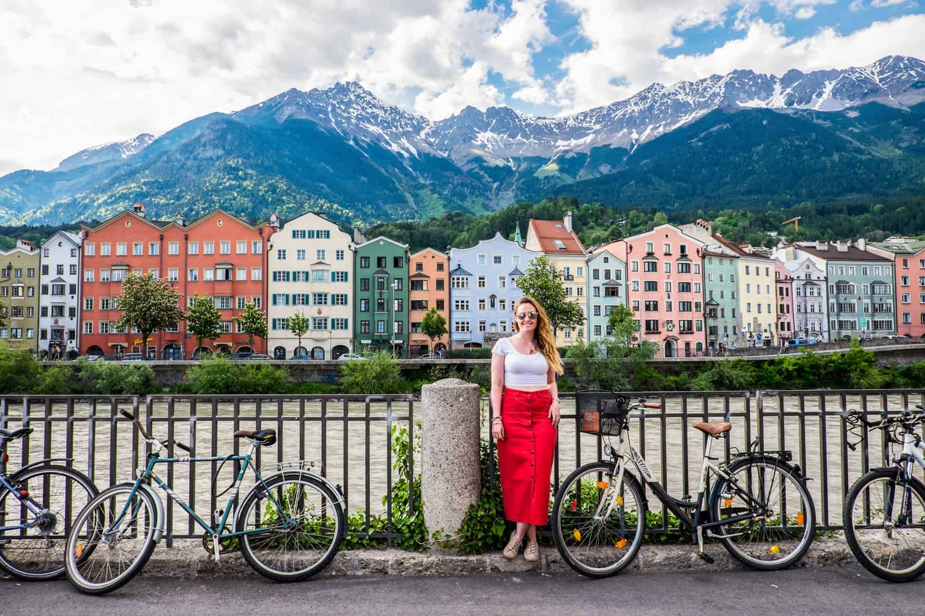 A woman in a red skirt stands in front of an iron railing, with the colourful houses along the Inn River in Innsbruck, Austria in the background