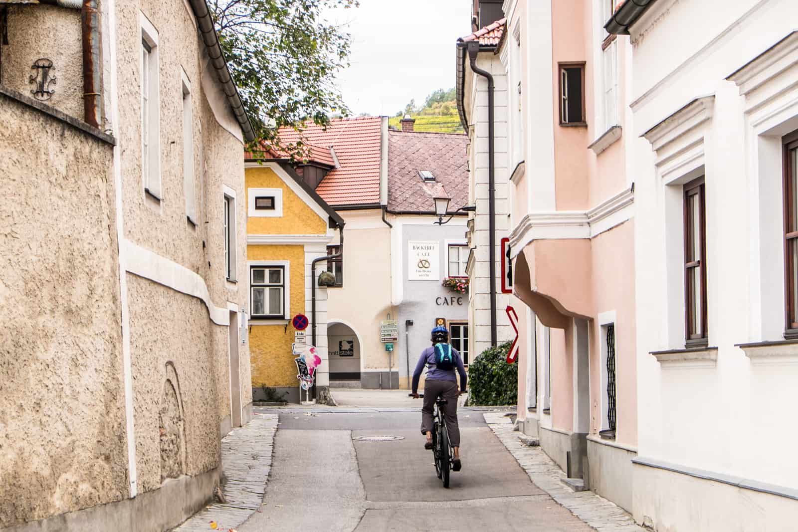 A woman cycles through the small and wonky pink and orange pastel buildings in Krems, Austria