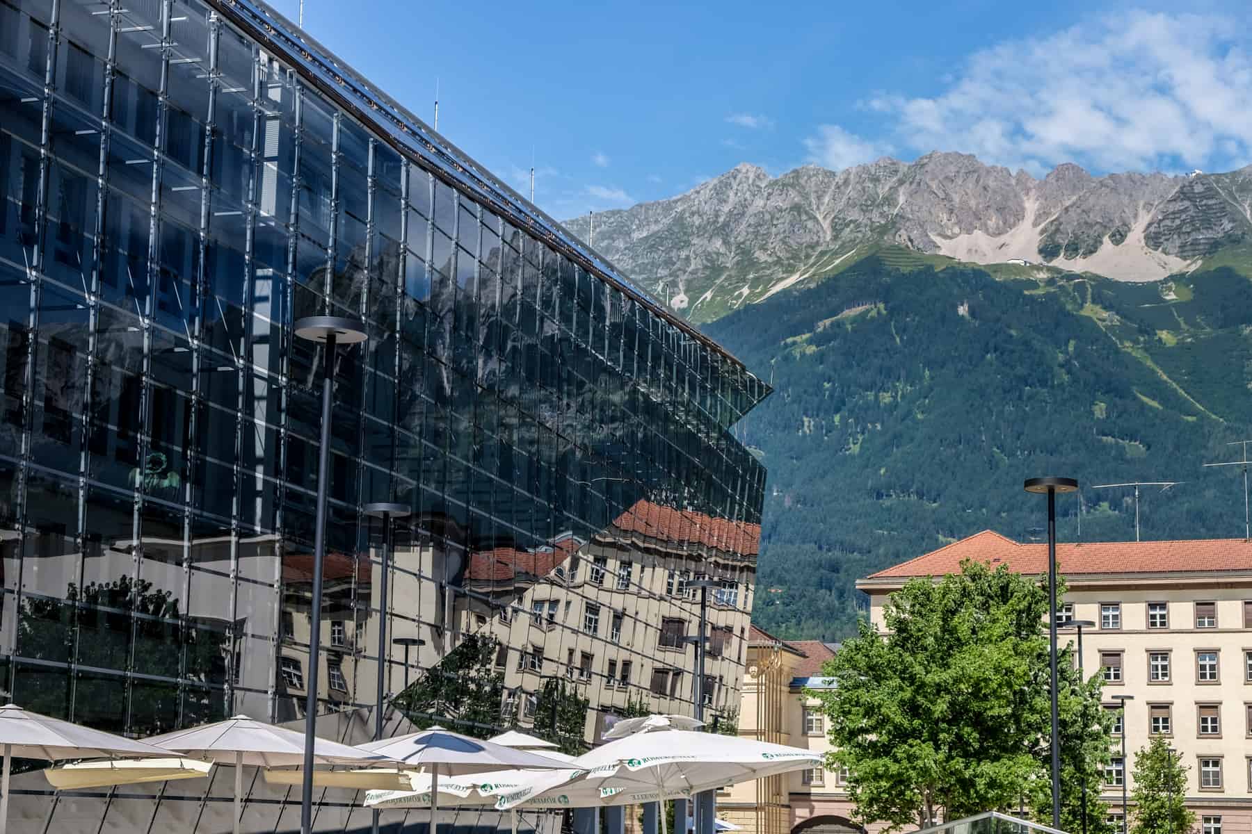 A glass building in Innsbruck reflects the mountains behind it, marking a merge of modern and nature