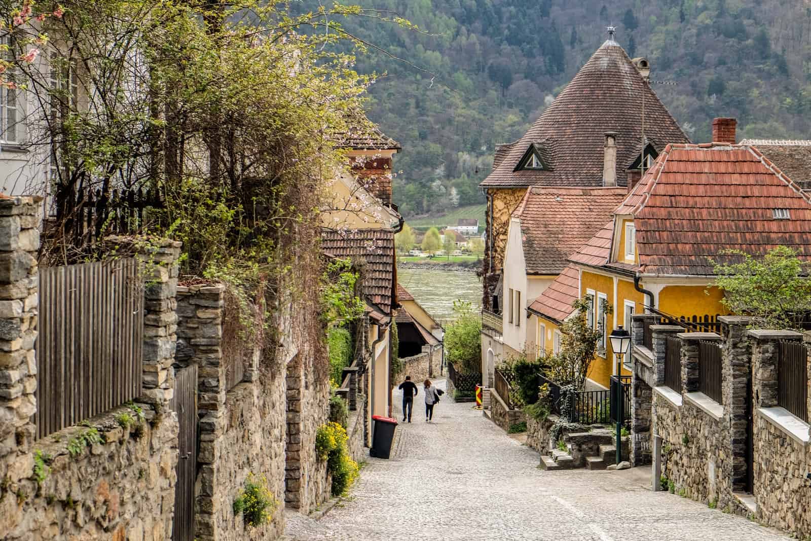 Small, red-roofed villages houses and the stone walls on a street leading down to the Danube River in Dürnstein