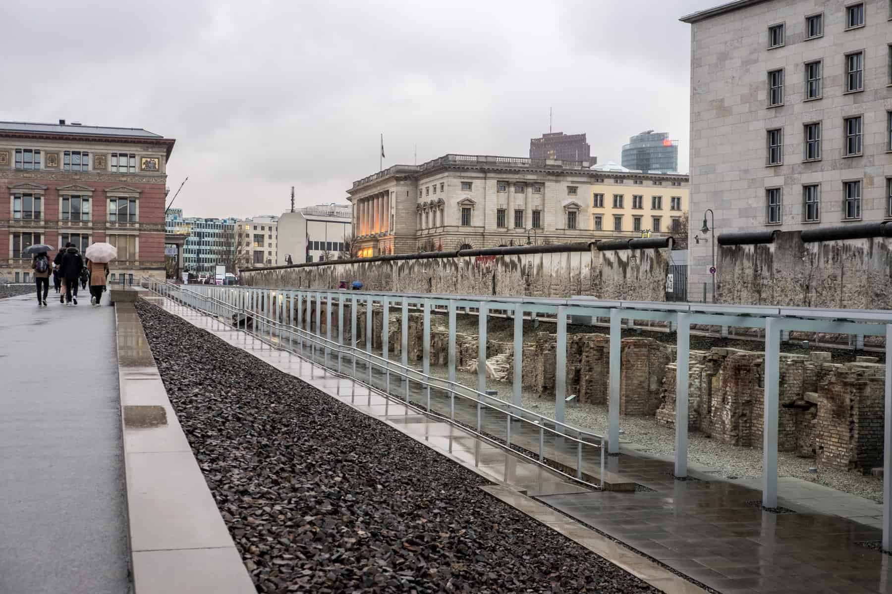 People in the distance walk past a remaining part of the Berlin Wall - part of an open air exhibition called the Topography of Terror