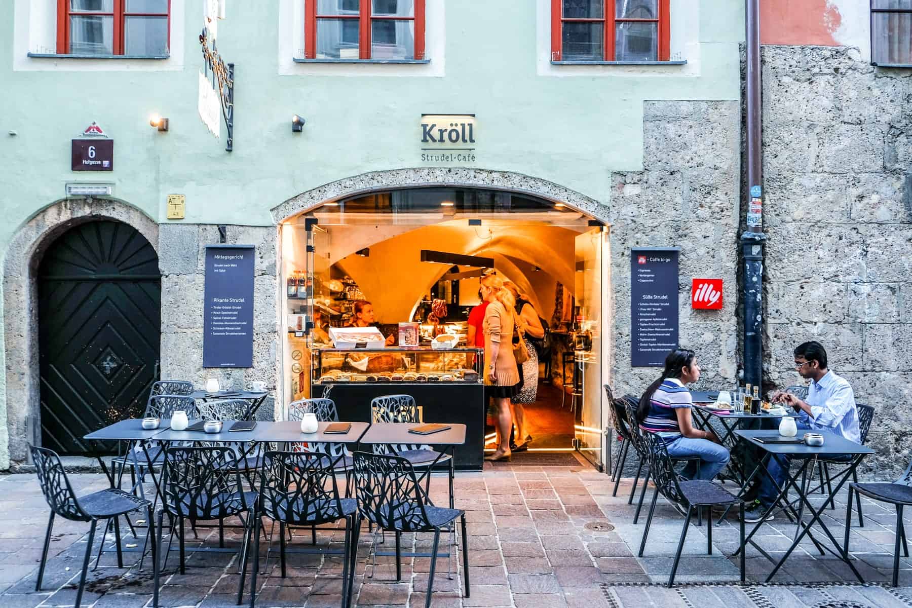 The golden lit entrance of Kröll Strudle cafe in Innsbruck, Austria with tables outside for dining