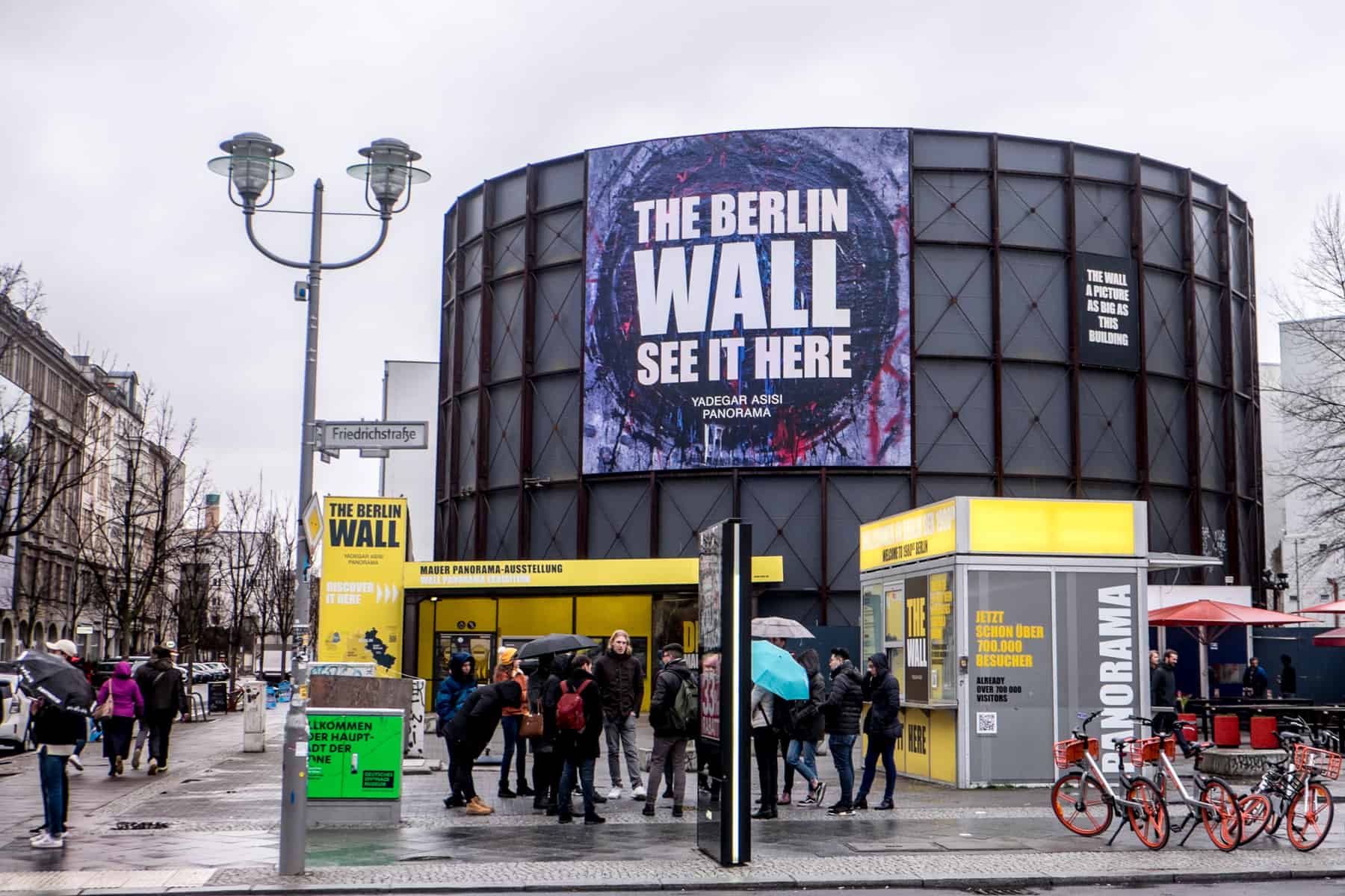 A large black barrel shape building with a purple Berlin Wall sign that houses a panorama image