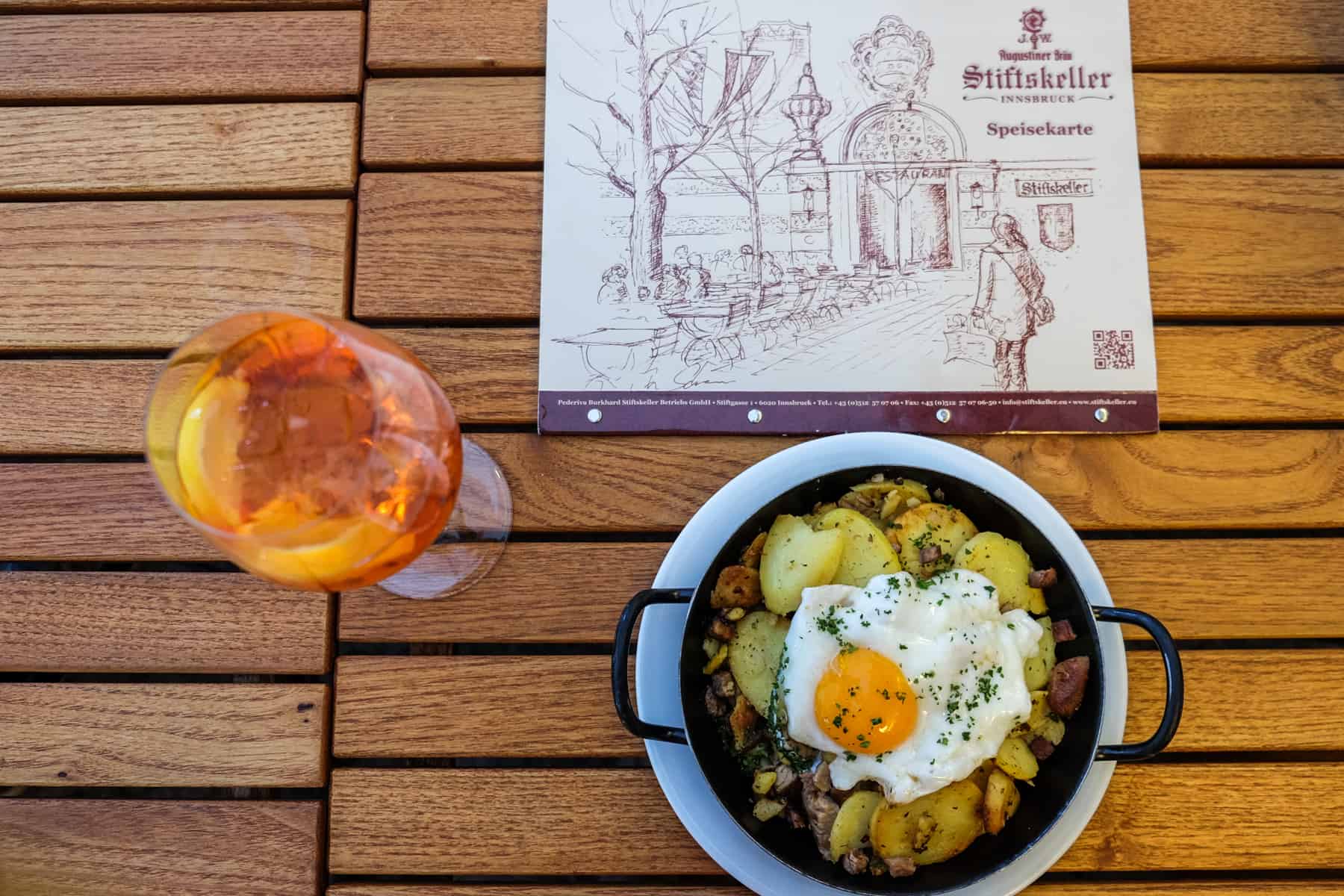 An iron plate of Tiroler Gröstl with meat, potatoes and egg, served on a wooden table at a traditional Austrian food restaurant in Innsbruck