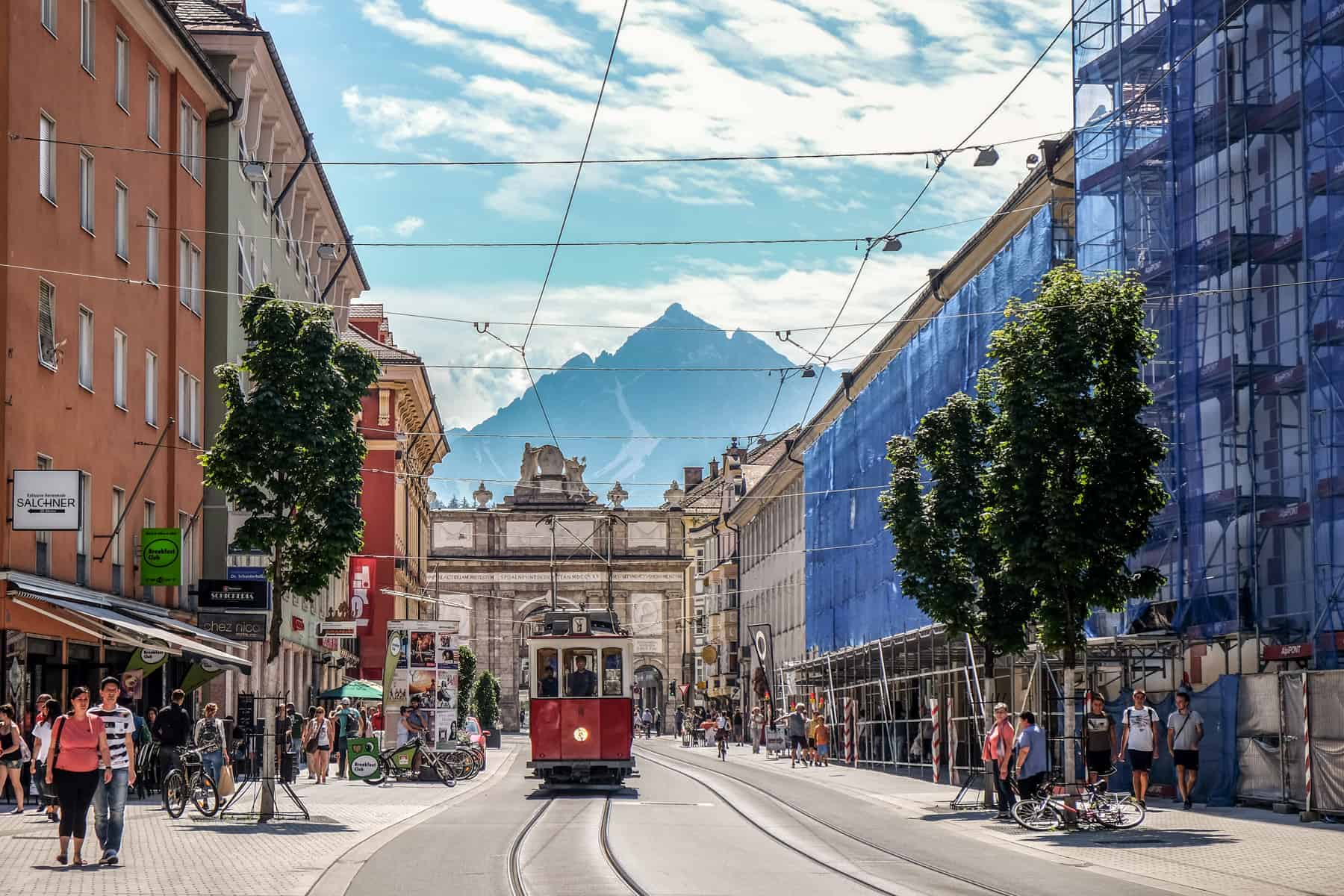 Street view of the Triumphal Arch in Innsbruck Old Town, Austria with a red tram travelling in the direction of the surrounding mountains