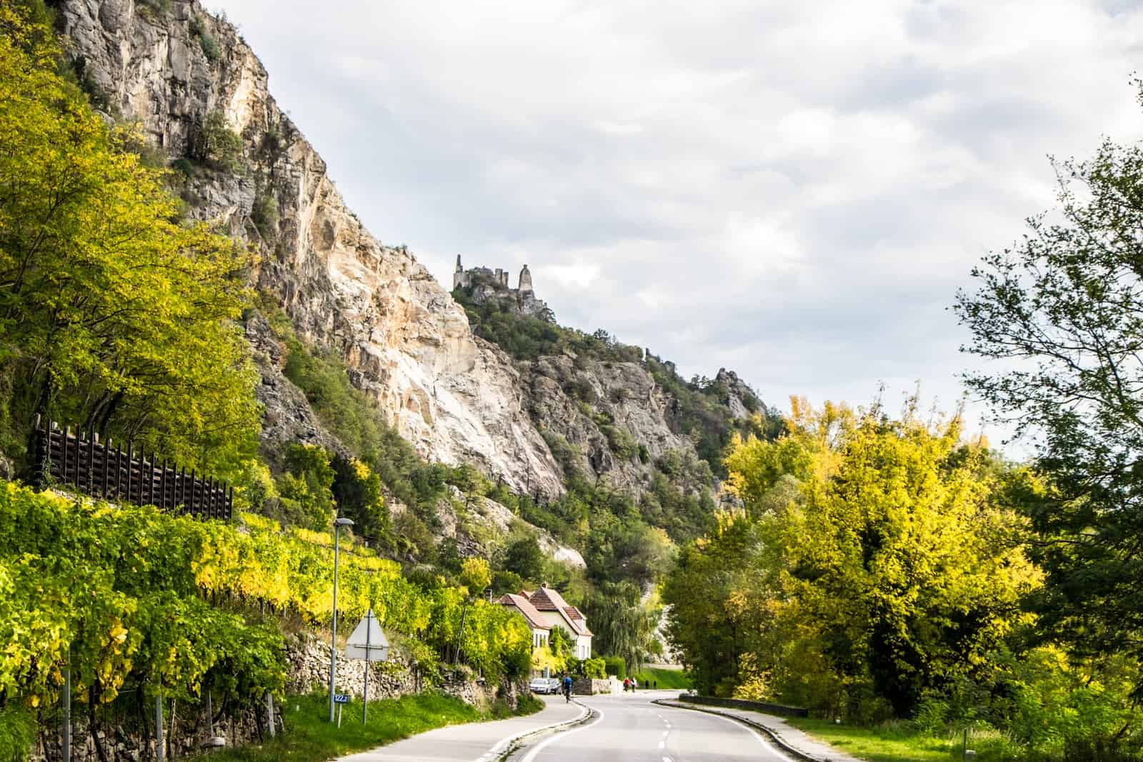 Far view of The Ruins of Dürnstein castle on the hillside, as seen from the main road passing the cliff face and green