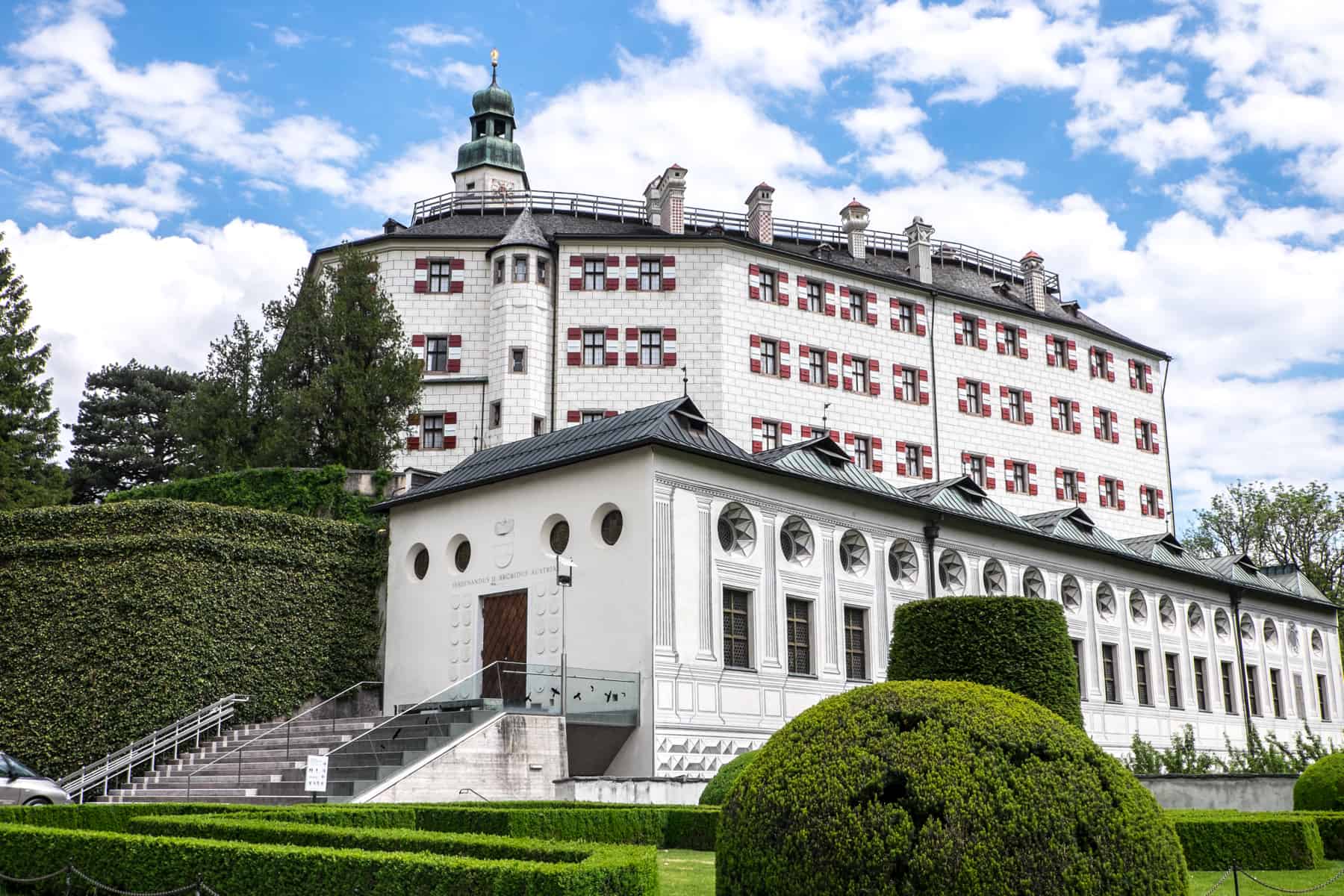 The white Exterior and Austria red and white flag window shutters of Ambras Castle in Innsbruck, Austria surrounded by manicured gardens