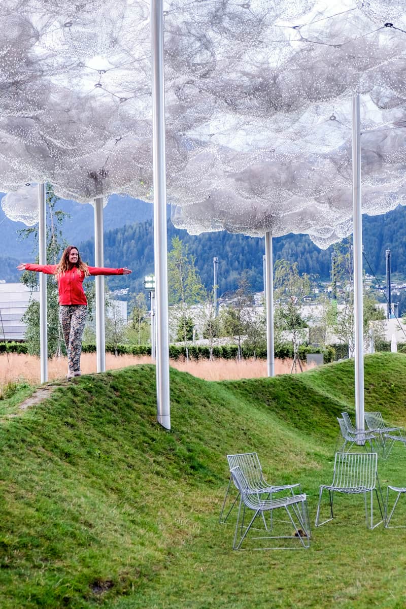 A woman in a red coat walks amongst the outdoor rain cloud art installation at Swarovski Crystal World in Innsbruck, Austria