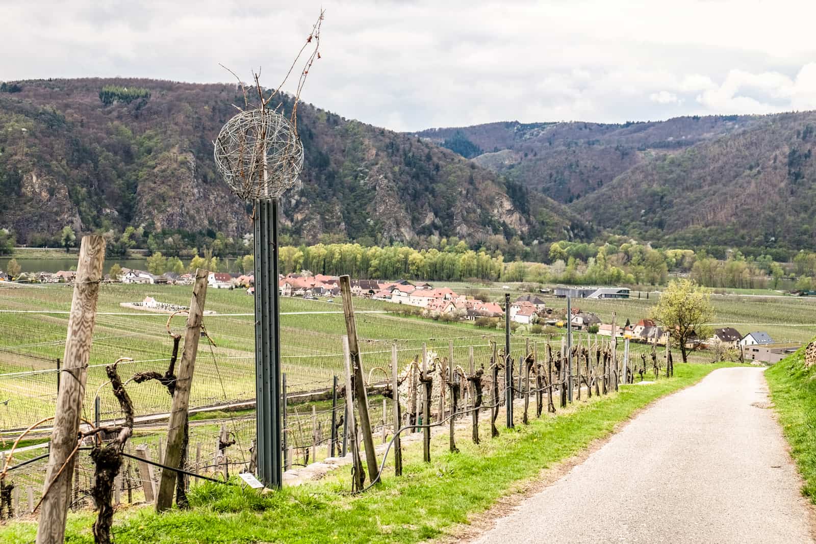 A pathway on The Wachau World Heritage Trail with a metal pole art sculpture to the left, leading down to a village marked by a cluster of houses