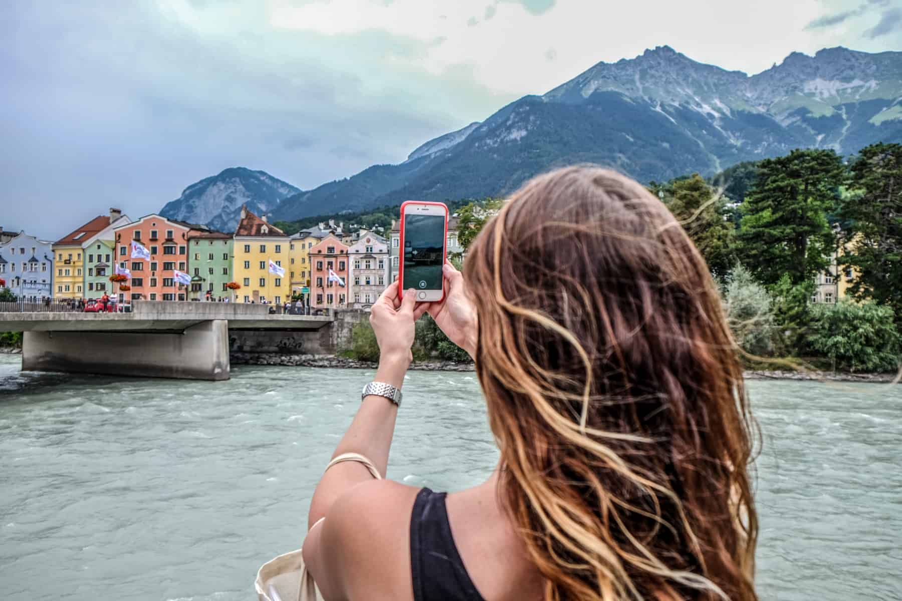 A woman takes a picture of Innsbruck colourful river houses on an iPhone