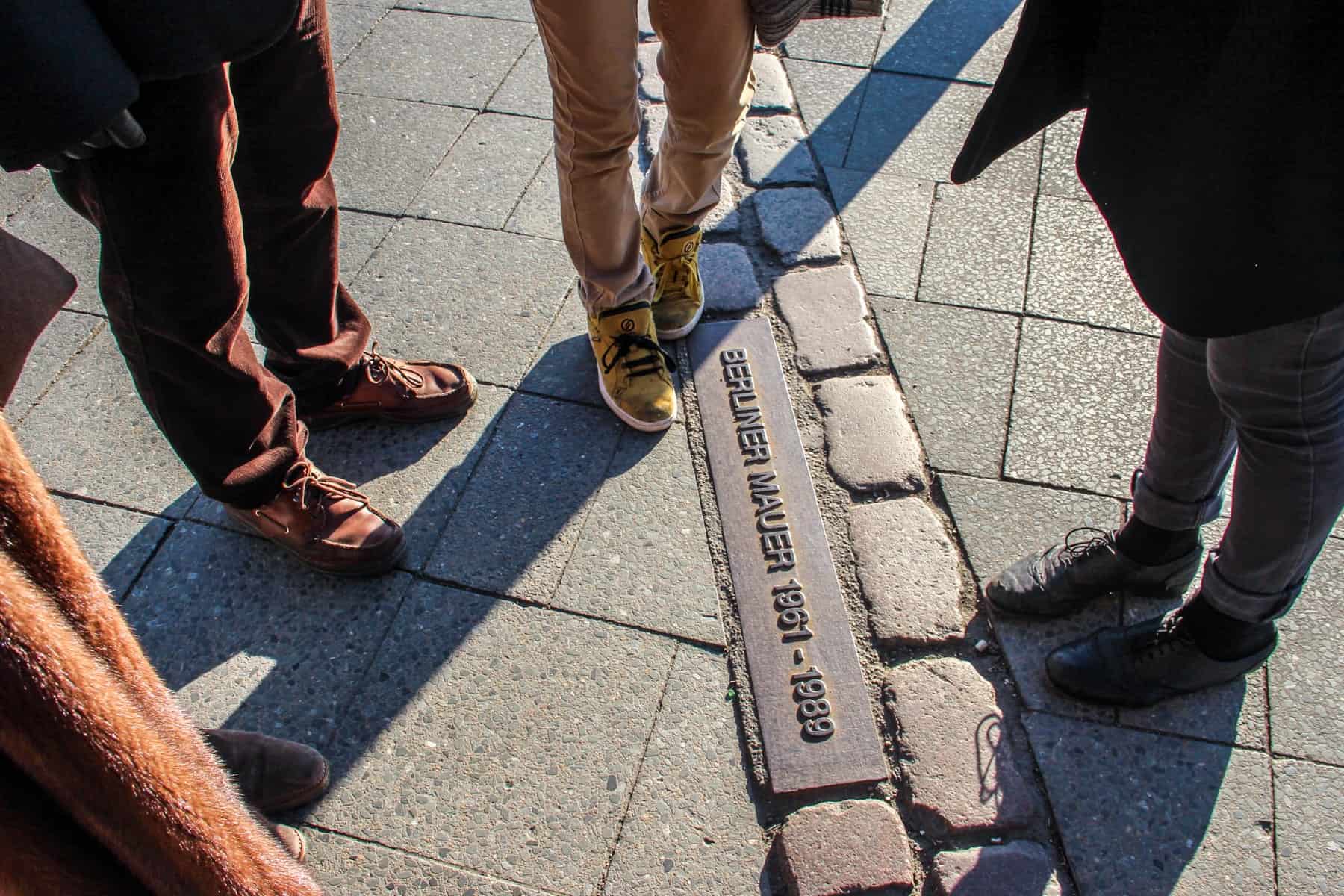 The feet of four tourists stand upon the double row of cobblestones that today mark the route of the Berlin Wall 