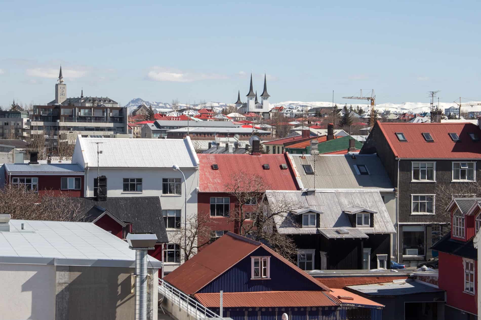 A cluster of houses painted in blue, red and green shades, and poking church spires in the city of Reykjavik, Iceland. 
