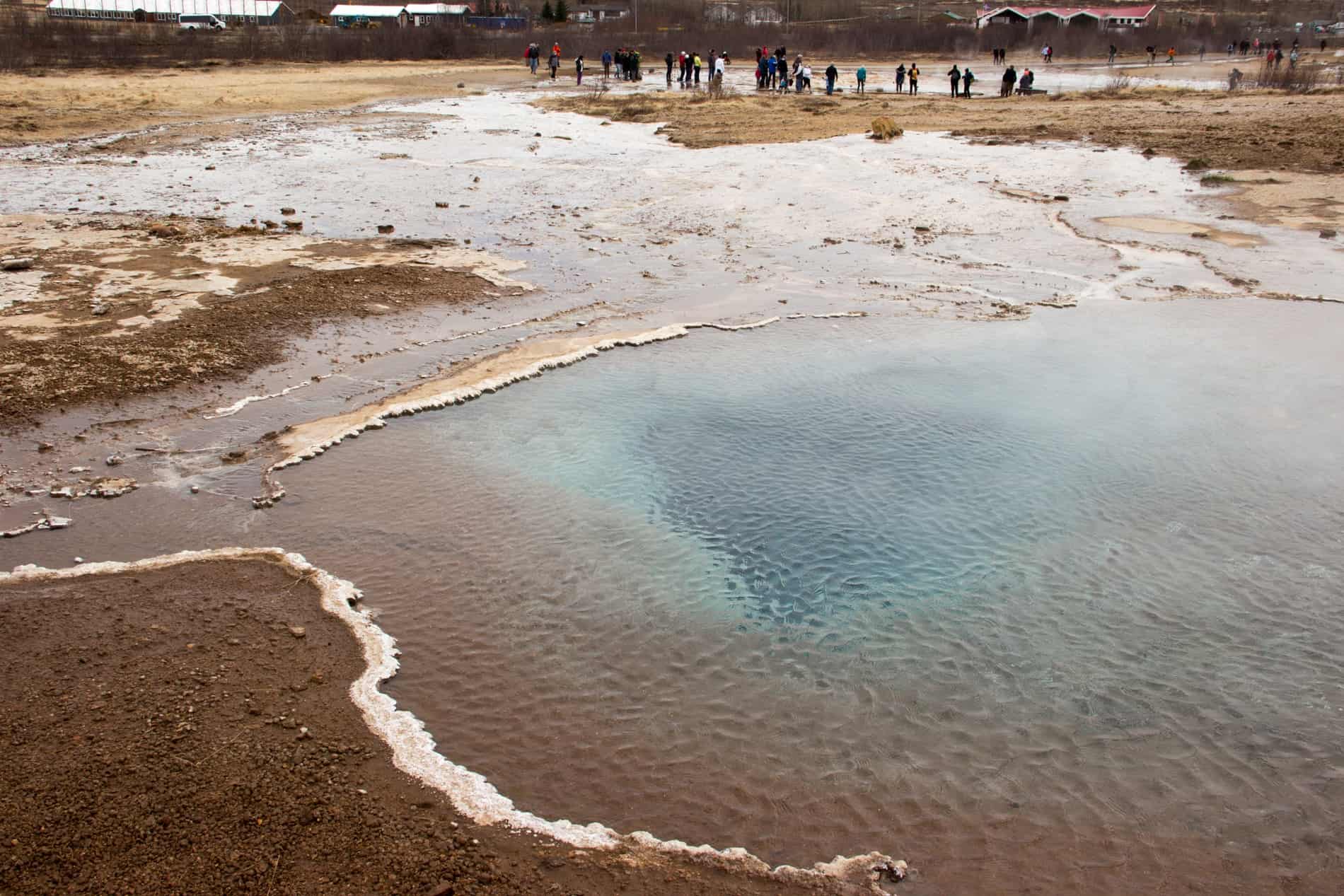 People standing near to the blue geothermal Geysir pool waters in a geothermal area in Iceland.