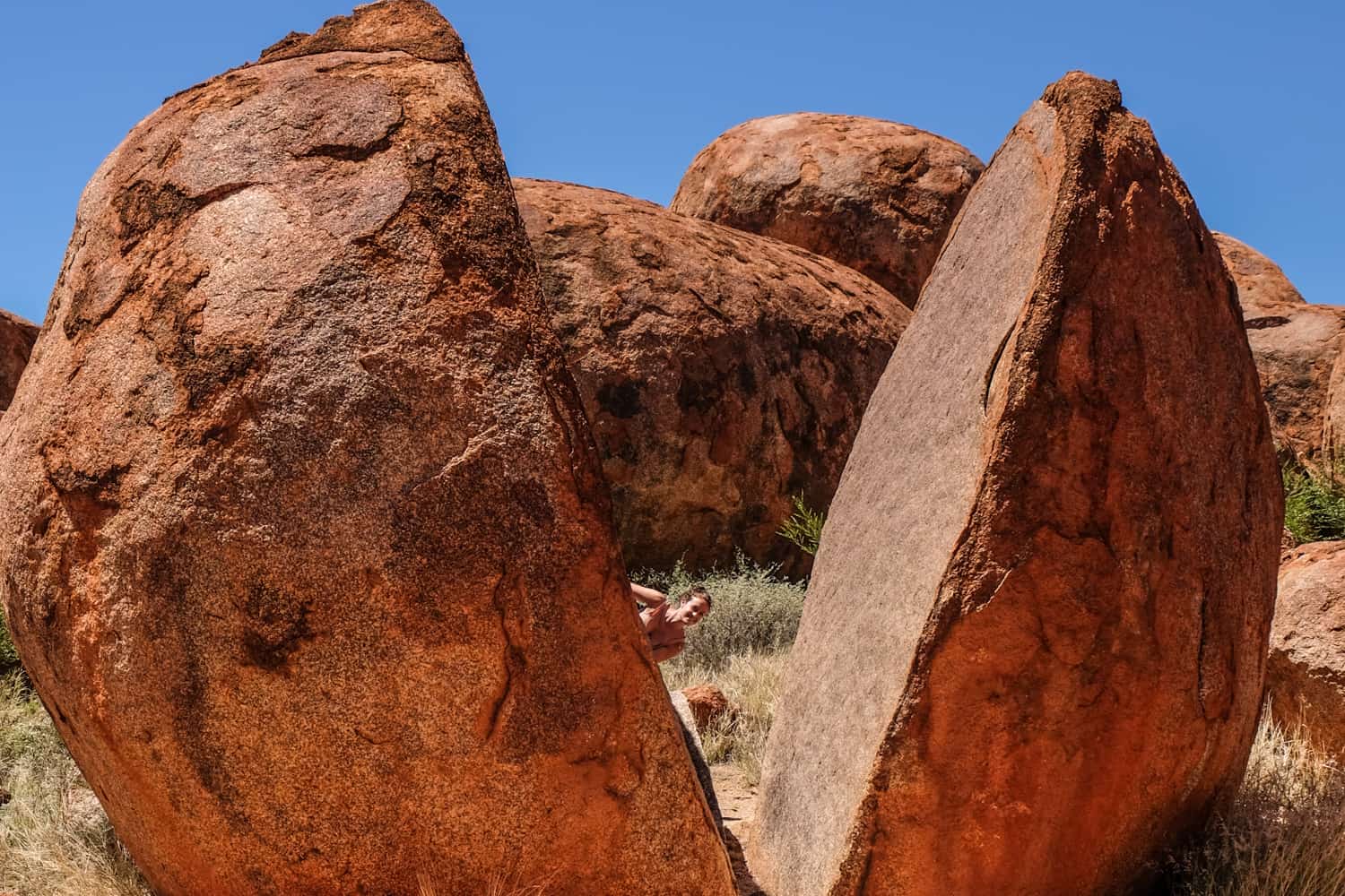 A woman peers through the opening of a round rock at the Devil's Marbles site, NT Australia. 