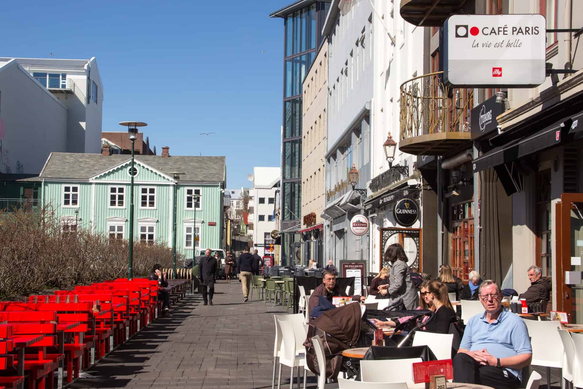 People sitting outside a cafe on a street with colourful buildings in Reykjavik, Iceland. 