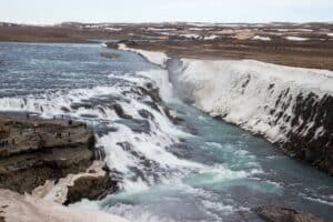 People gather on a rock viewpoint overlooking the huge blue casades of the Gullfoss Waterfall in Iceland.
