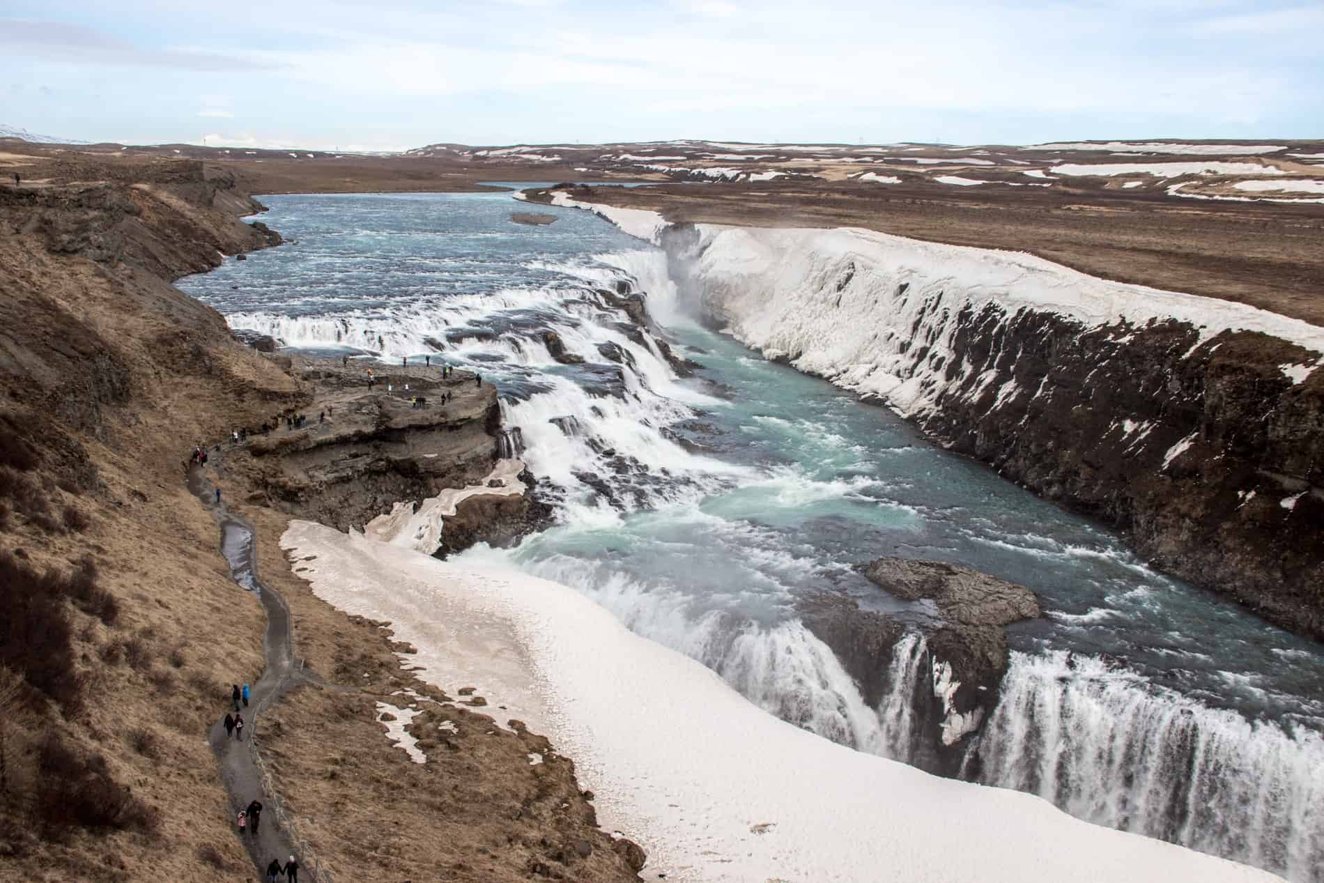 Elevated view of Gullfoss waterfall from a viewpoint overlooking the rock path walking trails next to the wild cascades. 