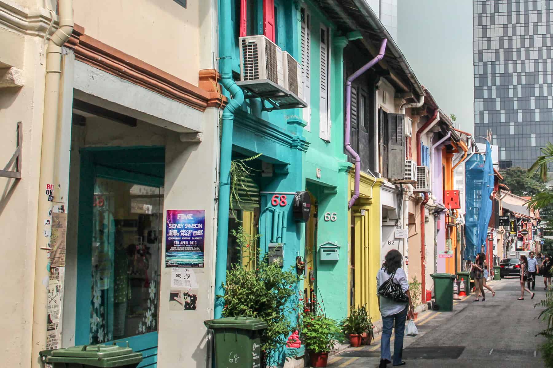 A woman walks past the mint green, yellow and orange shop colours on Haji Lane in Singapore that sit low in comparison to the tower block at the end of the street