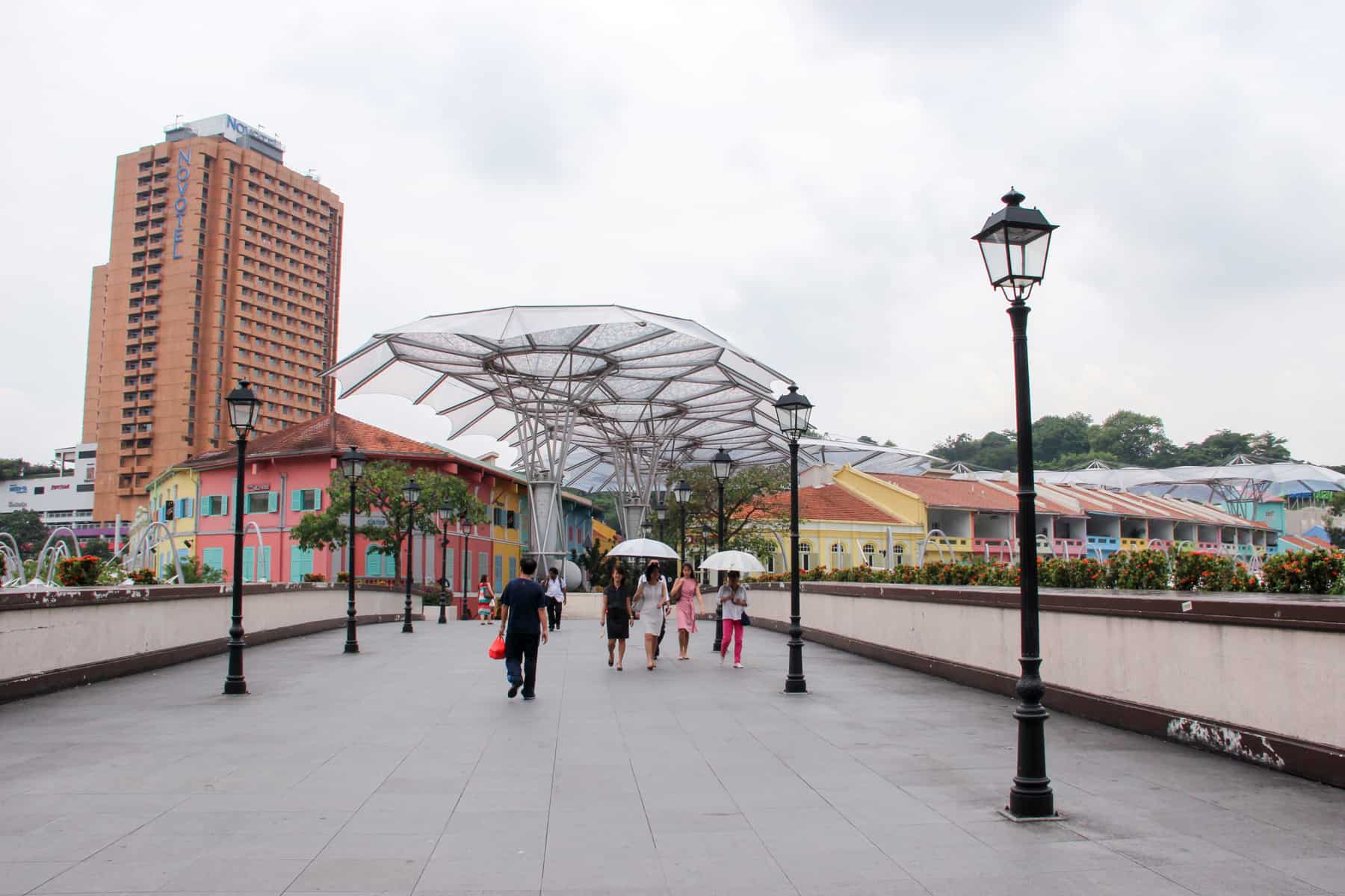 Five people, two holding umbrellas, walking towards some modern buildings in Singapore, the one on the path are shaped like metal trees