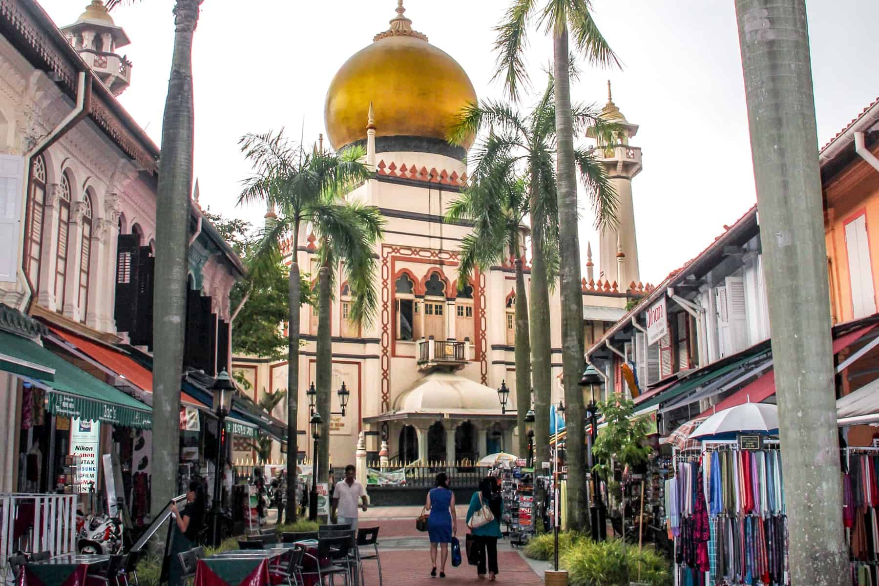 The gleaming cream exterior and gold onion shaped roof of the Masjid Sultan Mosque in Singapore that sits at the end of a shop and tree-lined street