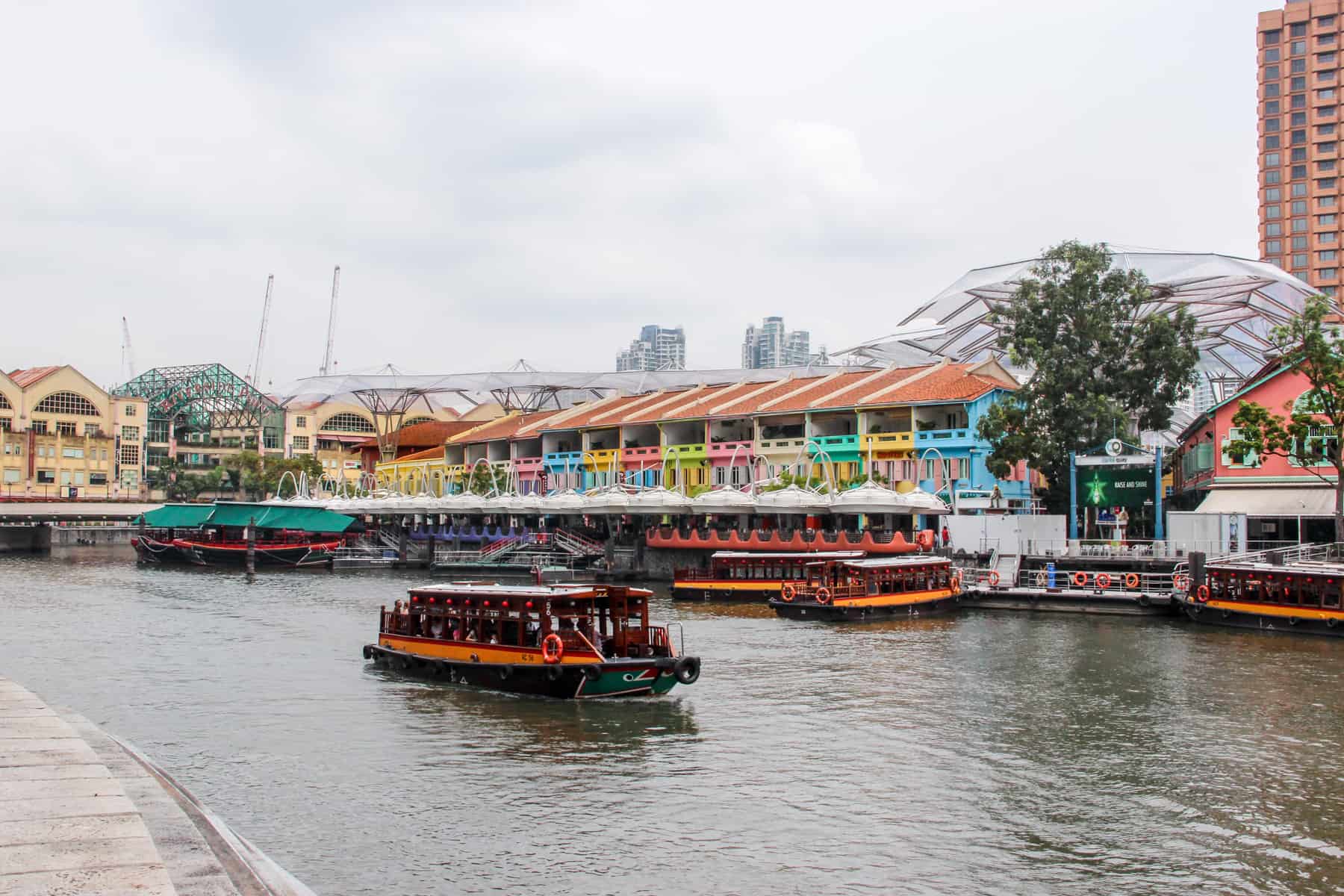 An orange boat passes the multicoloured rainbow row of waterside buildings in Singapore's Clarke Quay