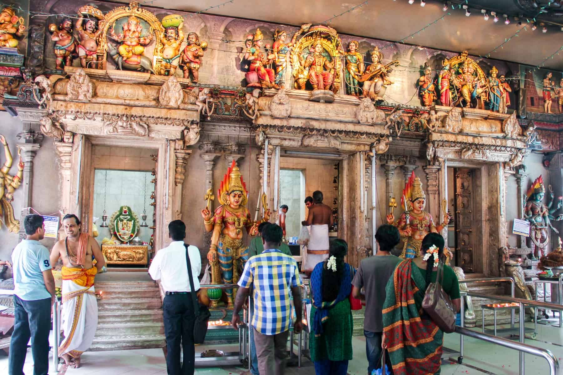 People pray inside the Sri Vadapathira Kaliamman temple in Singapore in front of three columned wall carvings, guarded by two Krishna statues