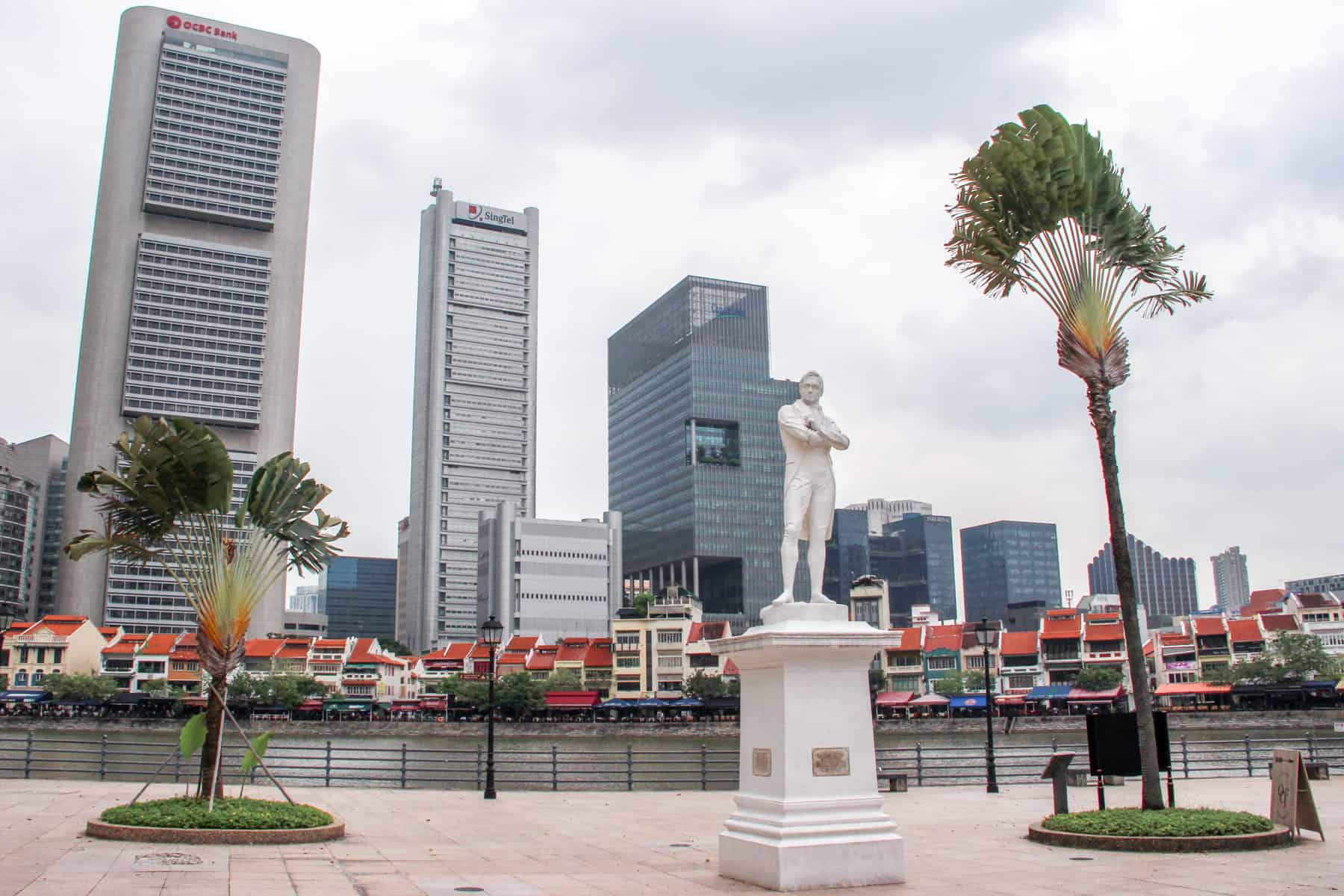 The white marble statue of Sir Raffles in Singapore that stands on the Singapore River waterside in front of the Civic District modern high rises that stand behind it